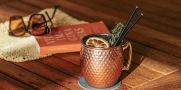 a copper mug with straws and a lemon slice on a wooden table