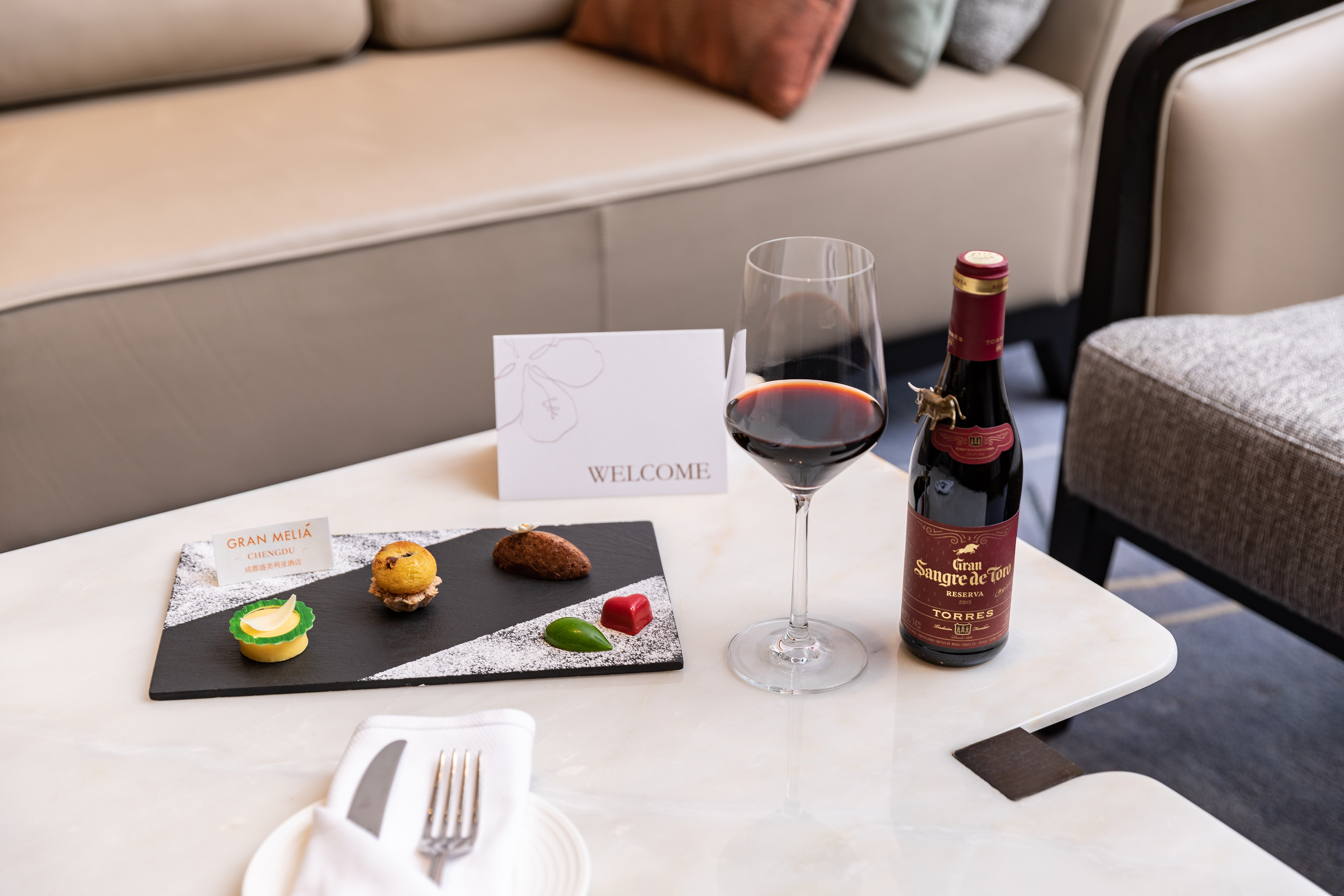 Gran Meliá Chengdu welcome amenity: red wine, glass, and small treats on slate.