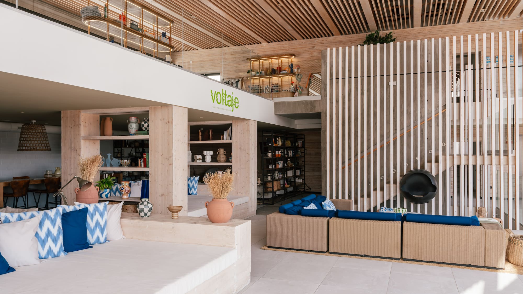 Modern lounge interior with wooden slatted ceiling, blue seating, and 'Voltaje' signage.
