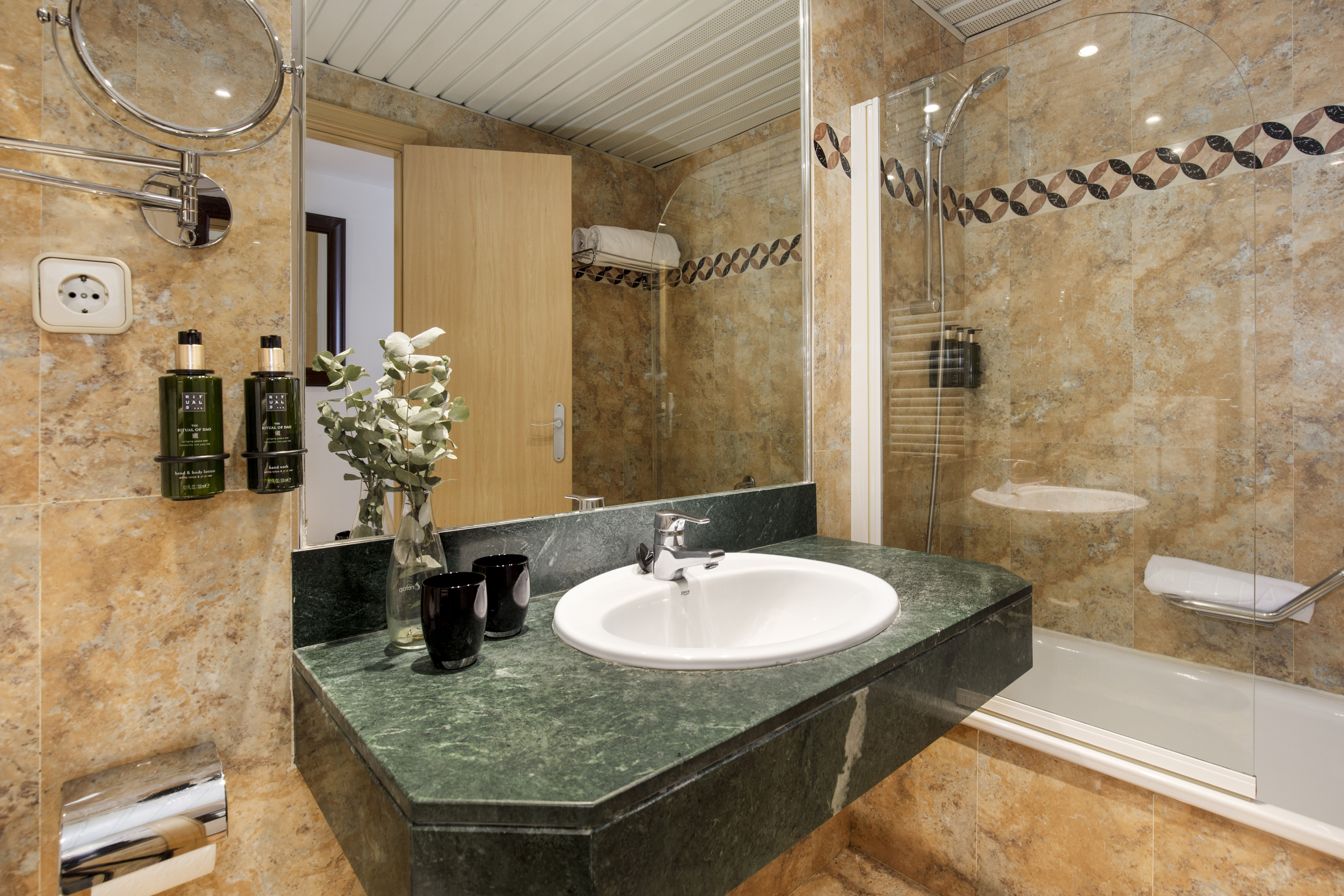 Modern hotel bathroom with green marble vanity, white sink, shower, and tiled walls.