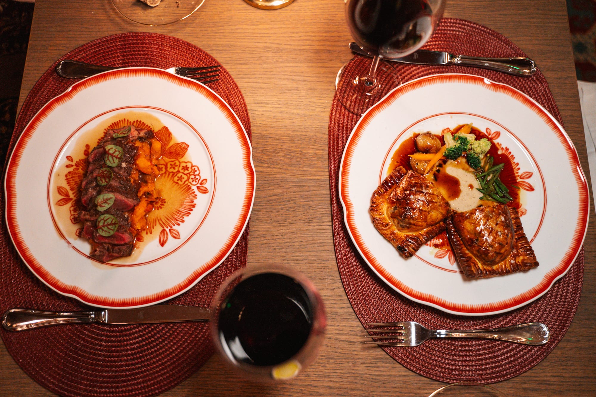Comida gourmet: bistec con puré y hojaldre con verduras, copas de vino.