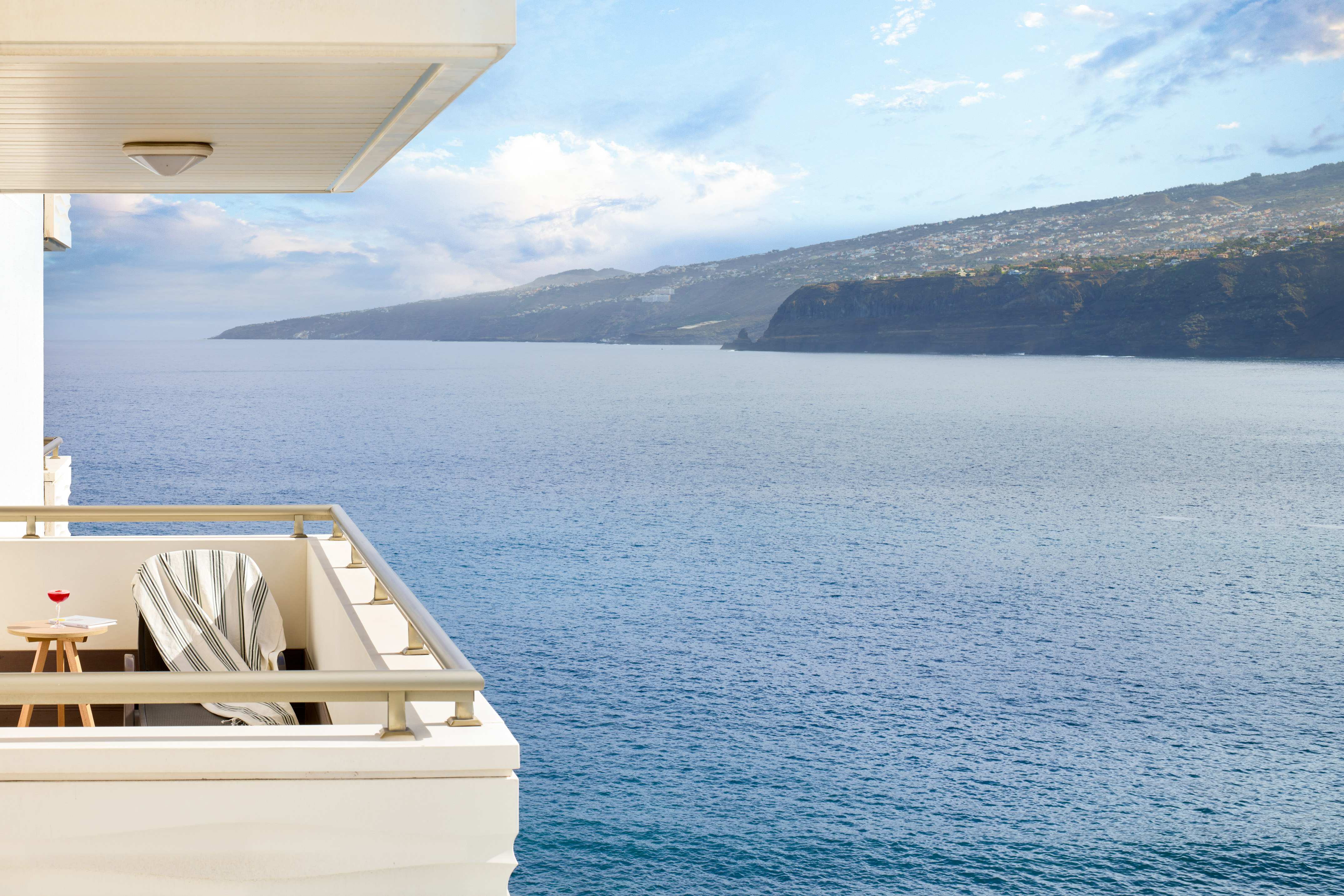 Balcony with ocean view, coastal mountains, and a distant town.