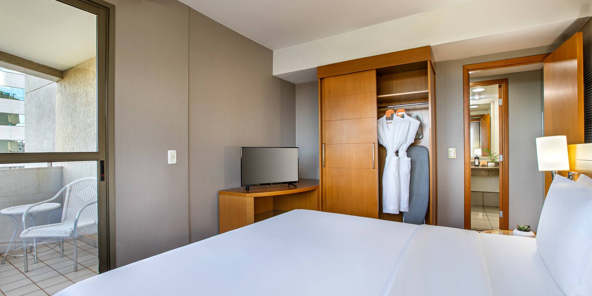 Modern hotel room with bed, TV, open closet, and balcony.