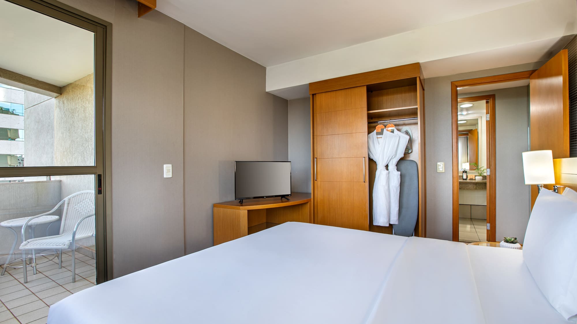 Modern hotel room with bed, TV, open closet, and balcony.