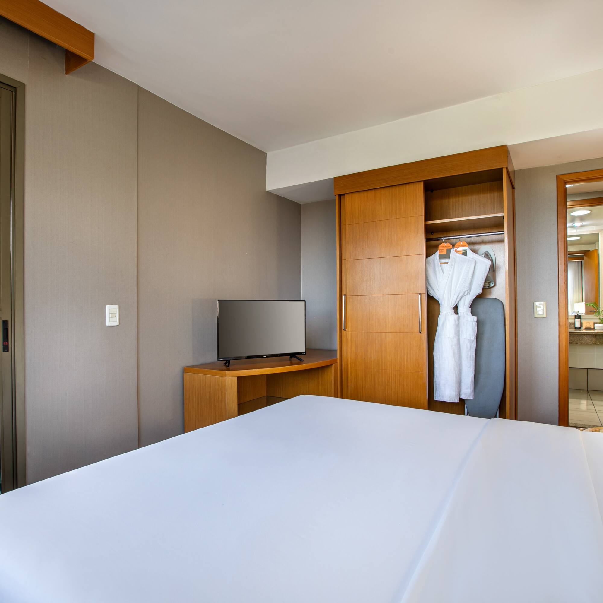 Modern hotel room with bed, TV, open closet, and balcony.