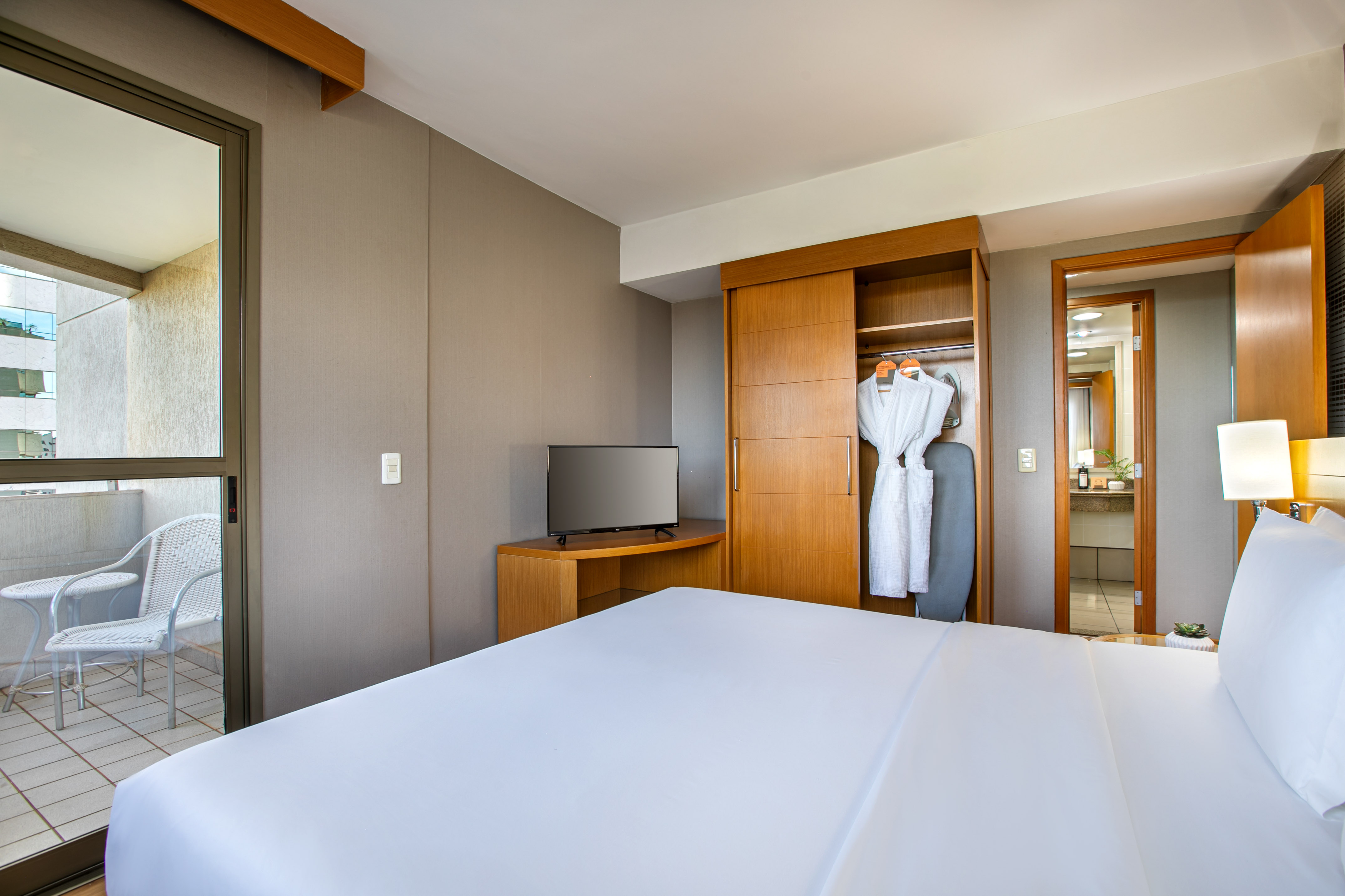 Modern hotel room with bed, TV, open closet, and balcony.
