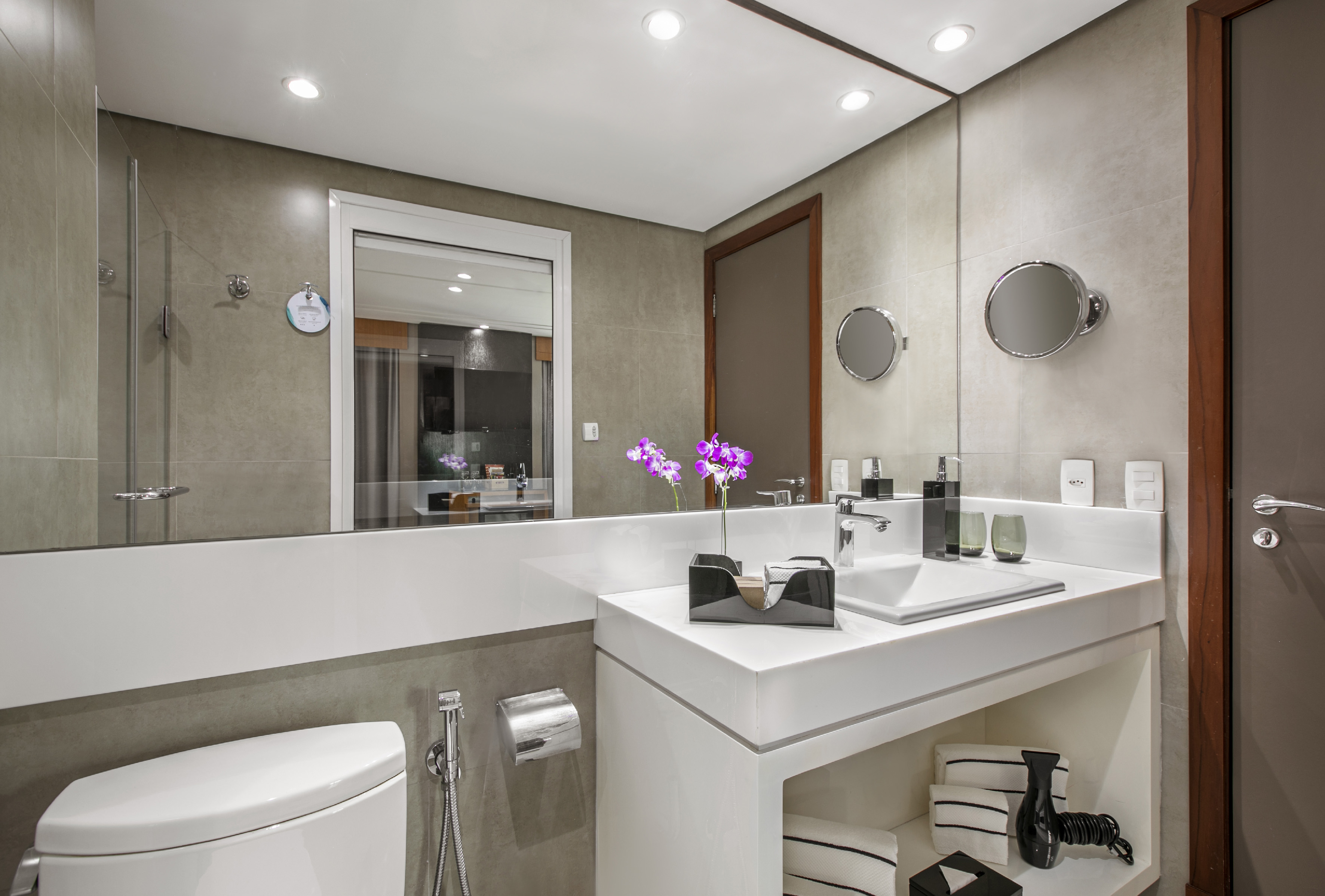 Modern bathroom with white vanity, sink, mirror, toilet, and purple orchid.
