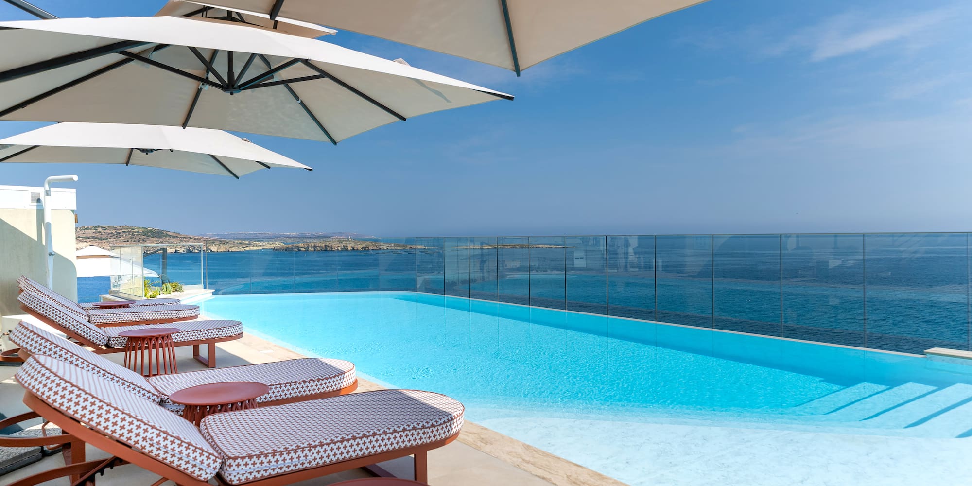 Infinity pool with ocean view, modern sun loungers, and white umbrellas.