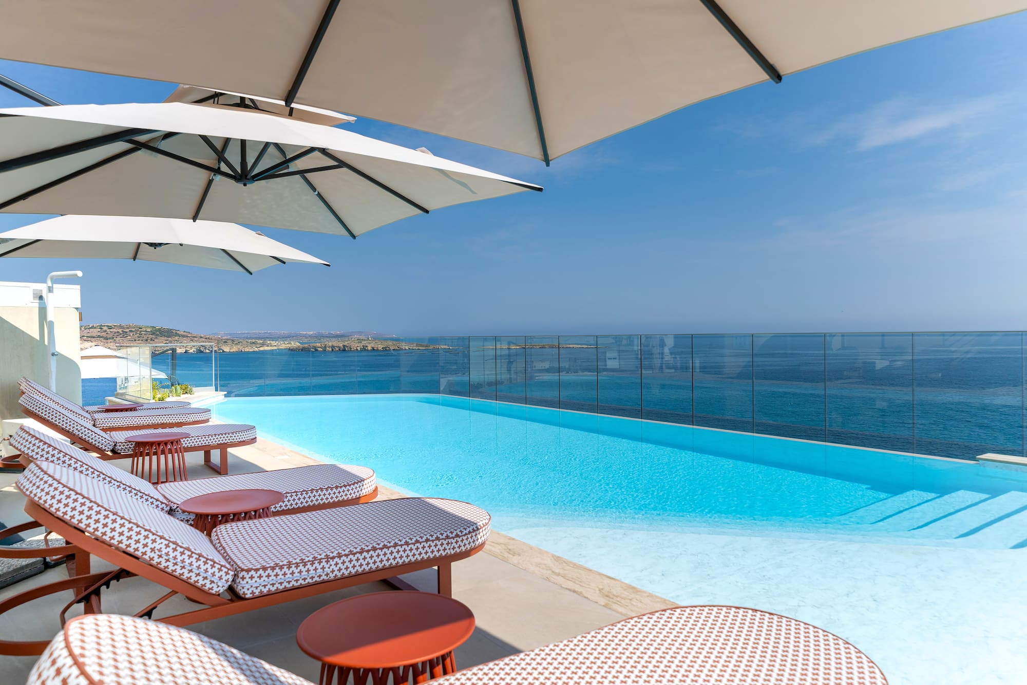 Luxury infinity pool with ocean view, lounge chairs, and sun umbrellas.