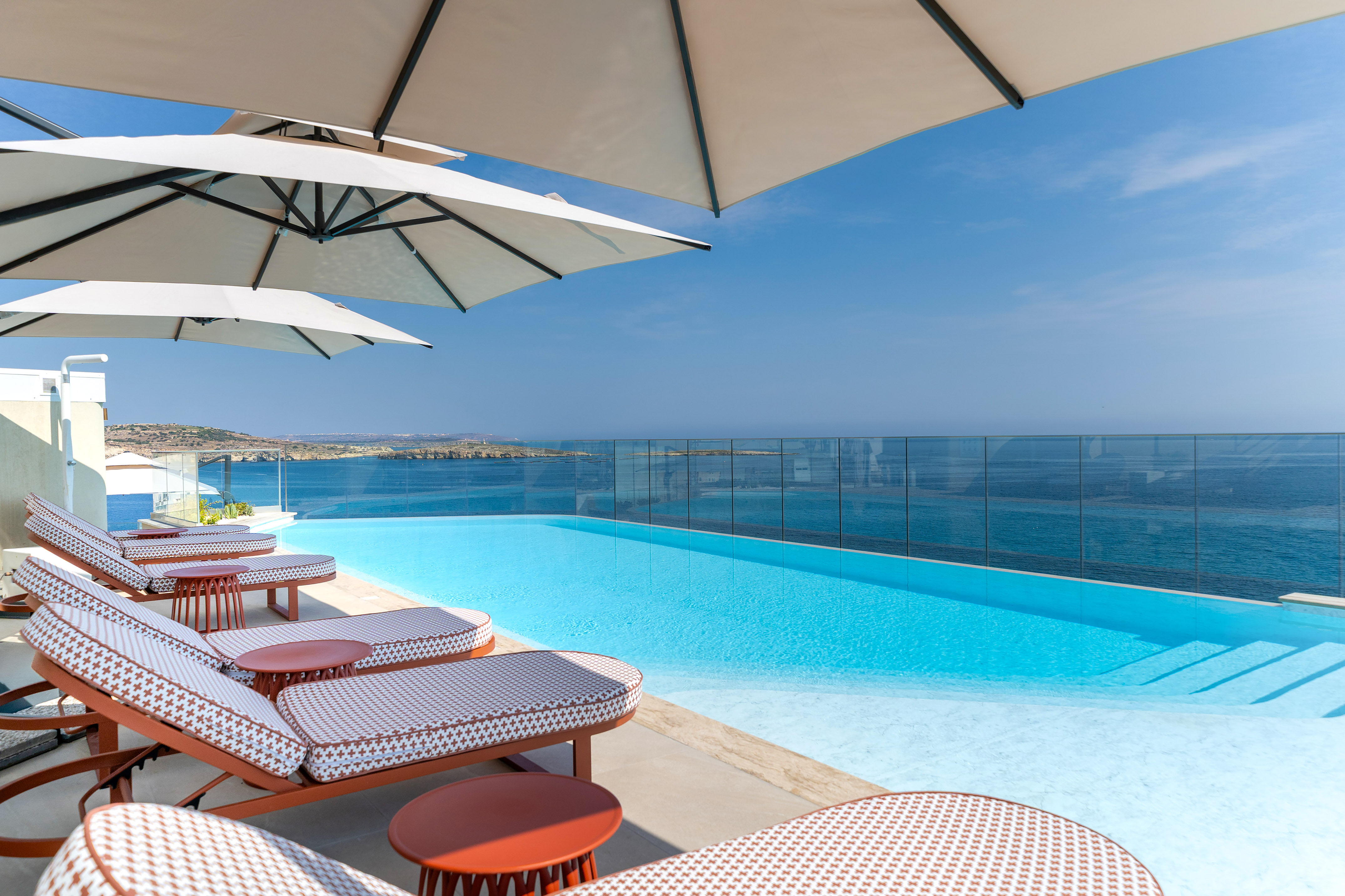 Luxury infinity pool with ocean view, lounge chairs, and sun umbrellas.
