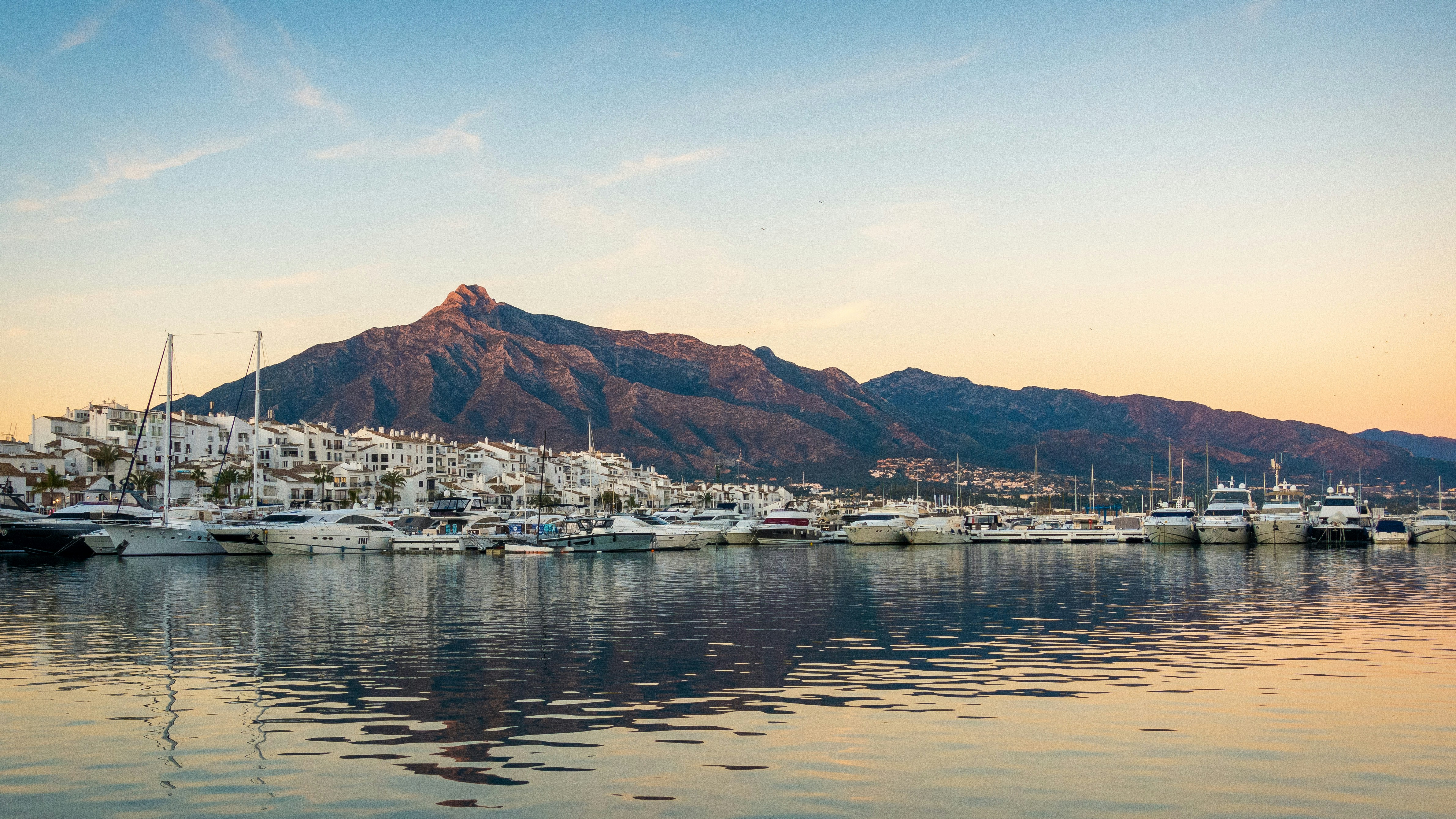 Puerto Banús marina with luxury yachts, white town, La Concha mountain at sunset.