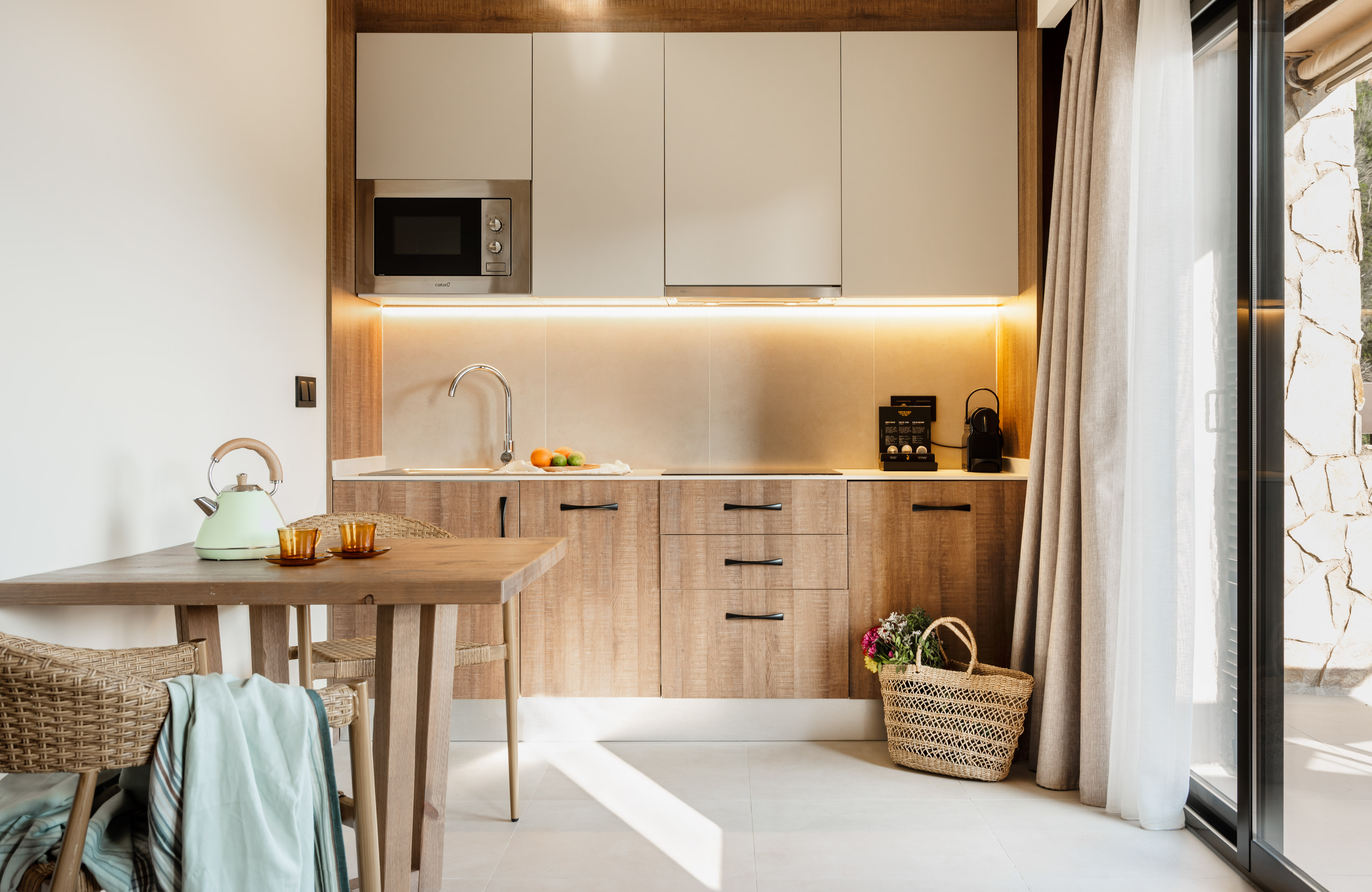 Modern kitchenette with wood cabinets, microwave, coffee machine, and dining table.