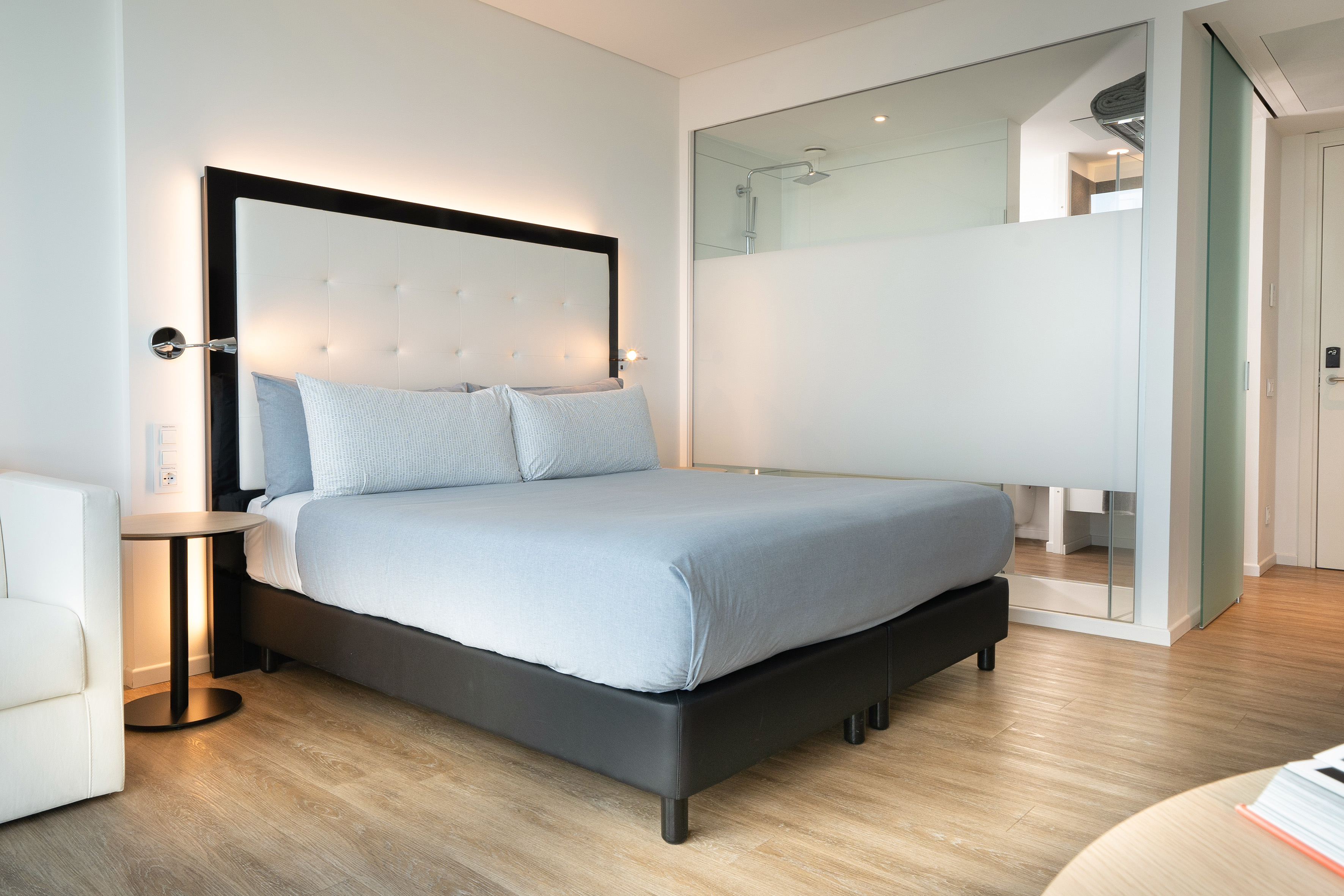 Modern hotel bedroom with white tufted headboard, king bed, and glass shower.