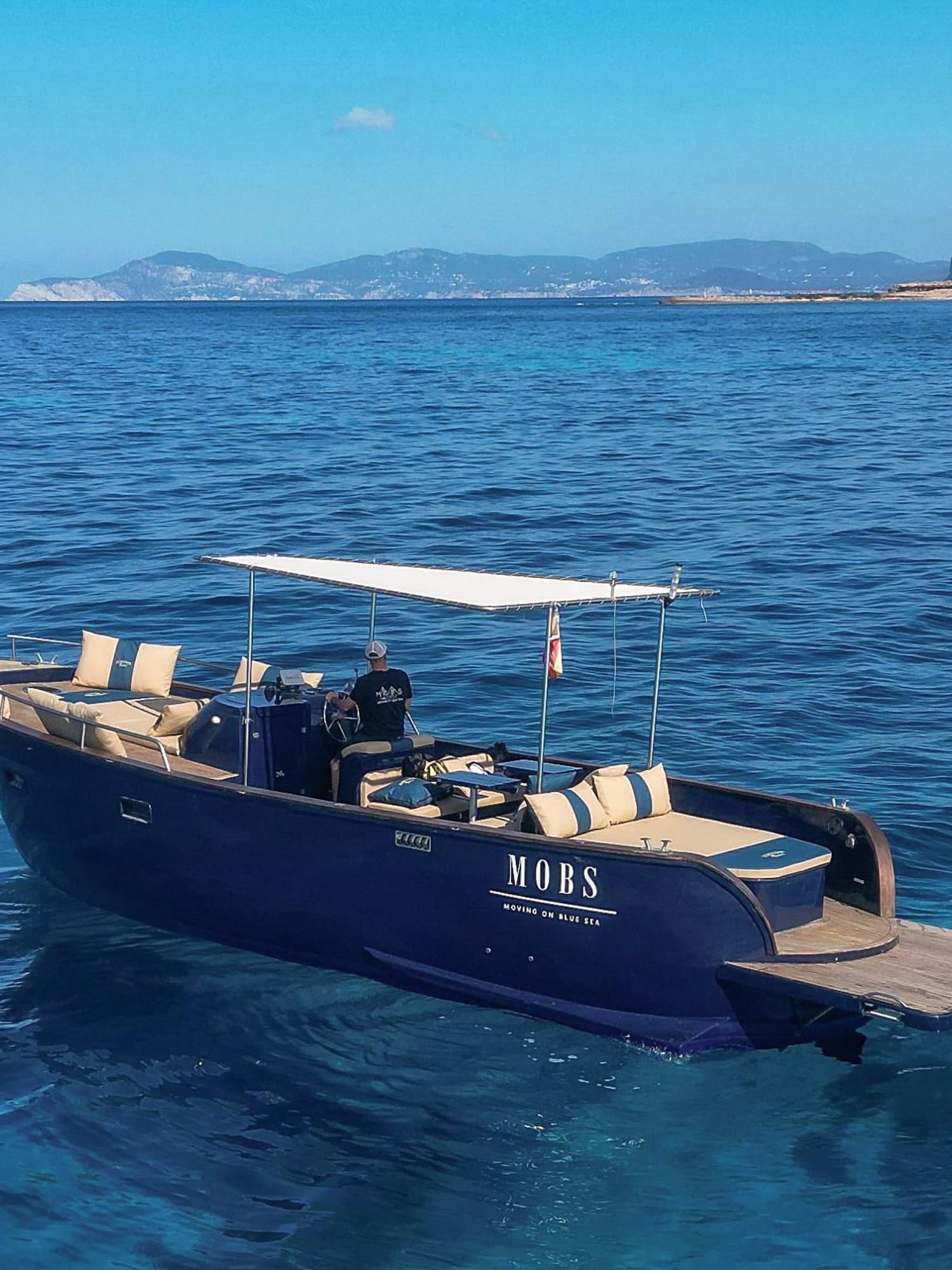 Lancha MOBS azul en mar cristalino cerca de Ibiza, patrón al mando.