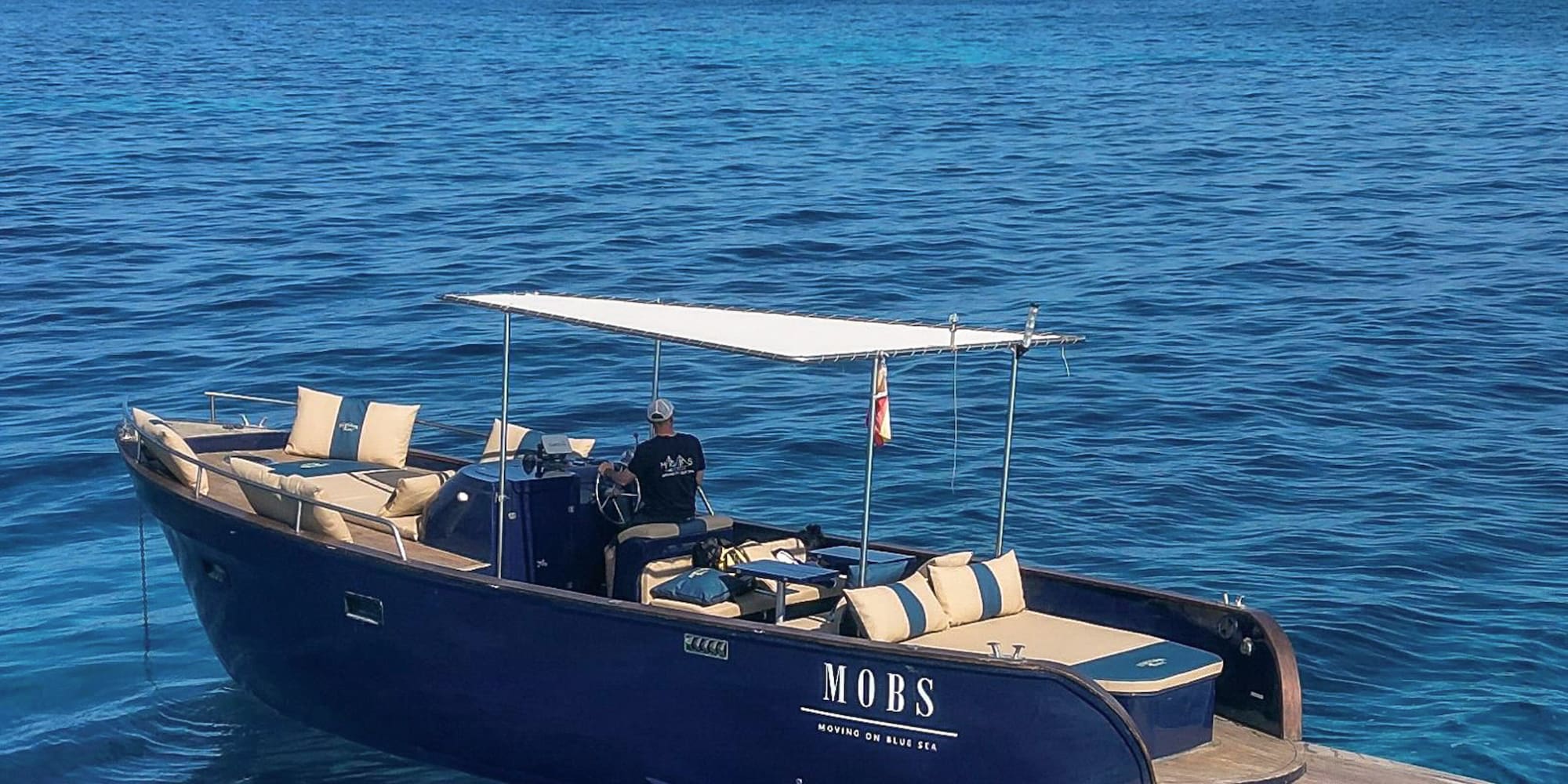 Lancha MOBS azul en mar cristalino cerca de Ibiza, patrón al mando.