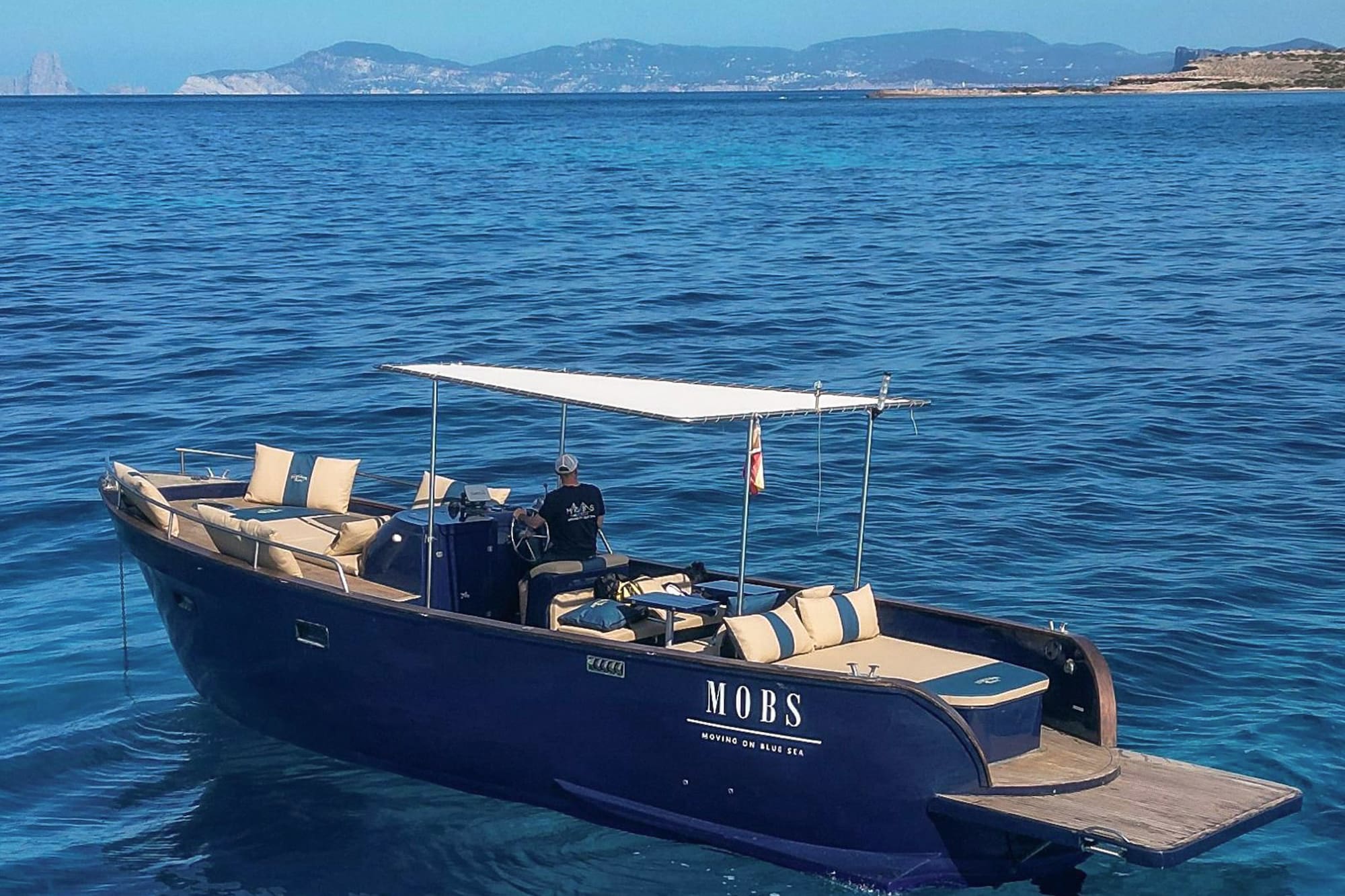 Lancha MOBS azul en mar cristalino cerca de Ibiza, patrón al mando.