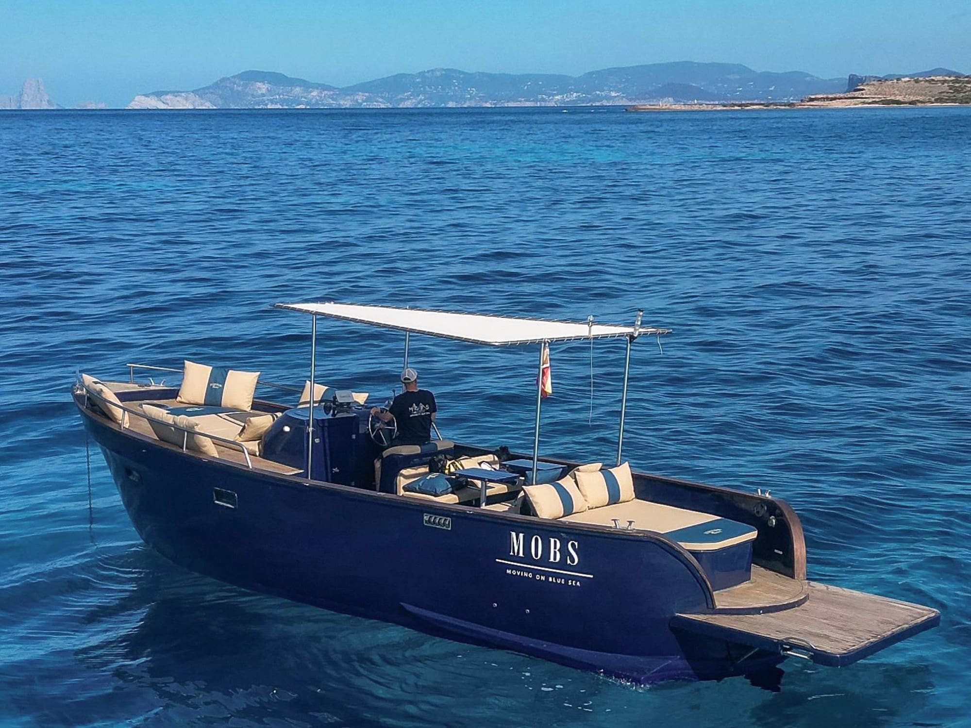 Lancha MOBS azul en mar cristalino cerca de Ibiza, patrón al mando.
