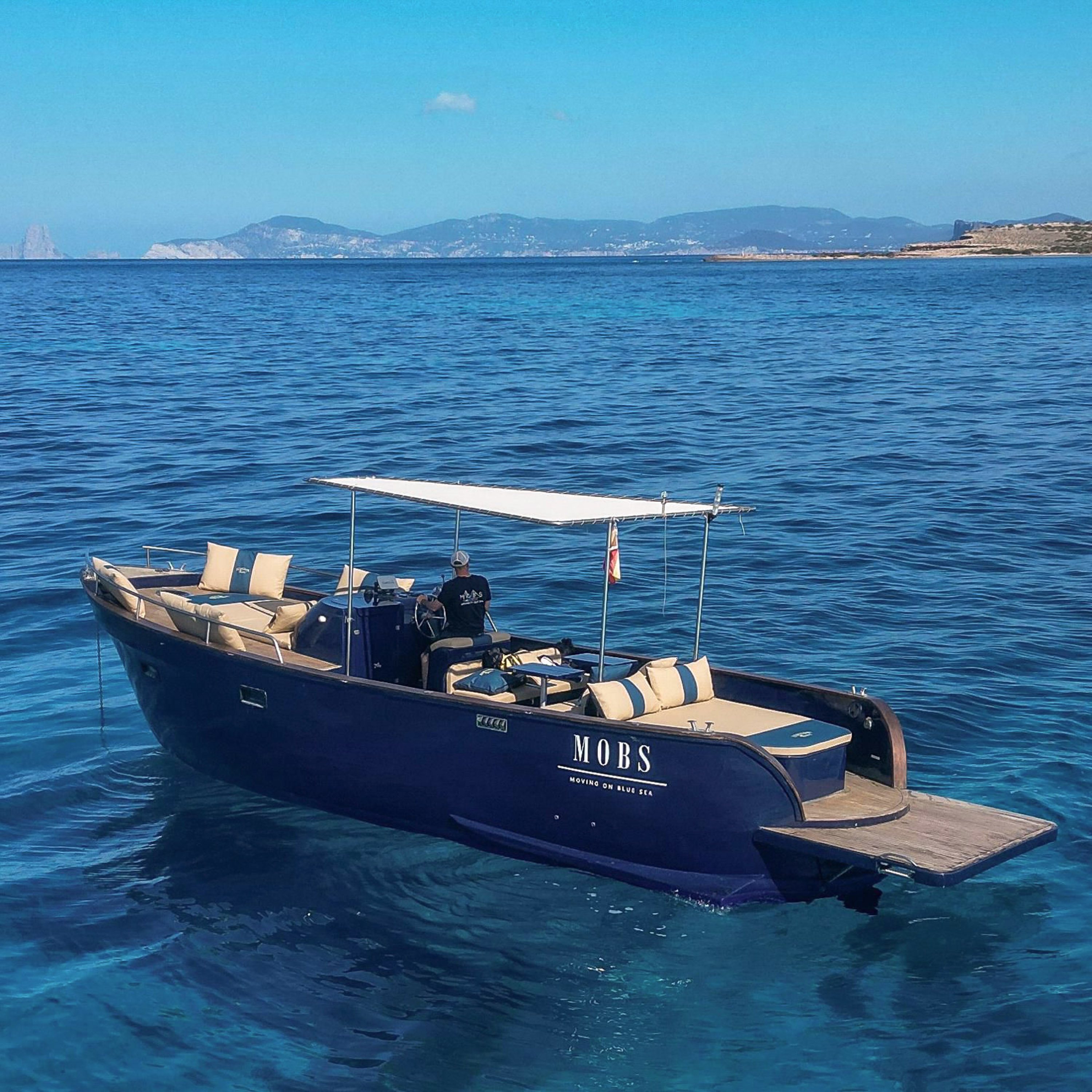 Lancha MOBS azul en mar cristalino cerca de Ibiza, patrón al mando.