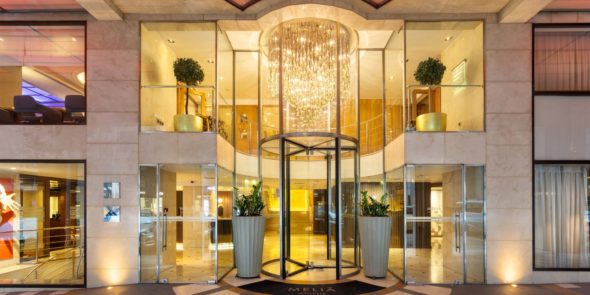 Meliá Athens luxury hotel entrance with revolving door and glowing chandelier.