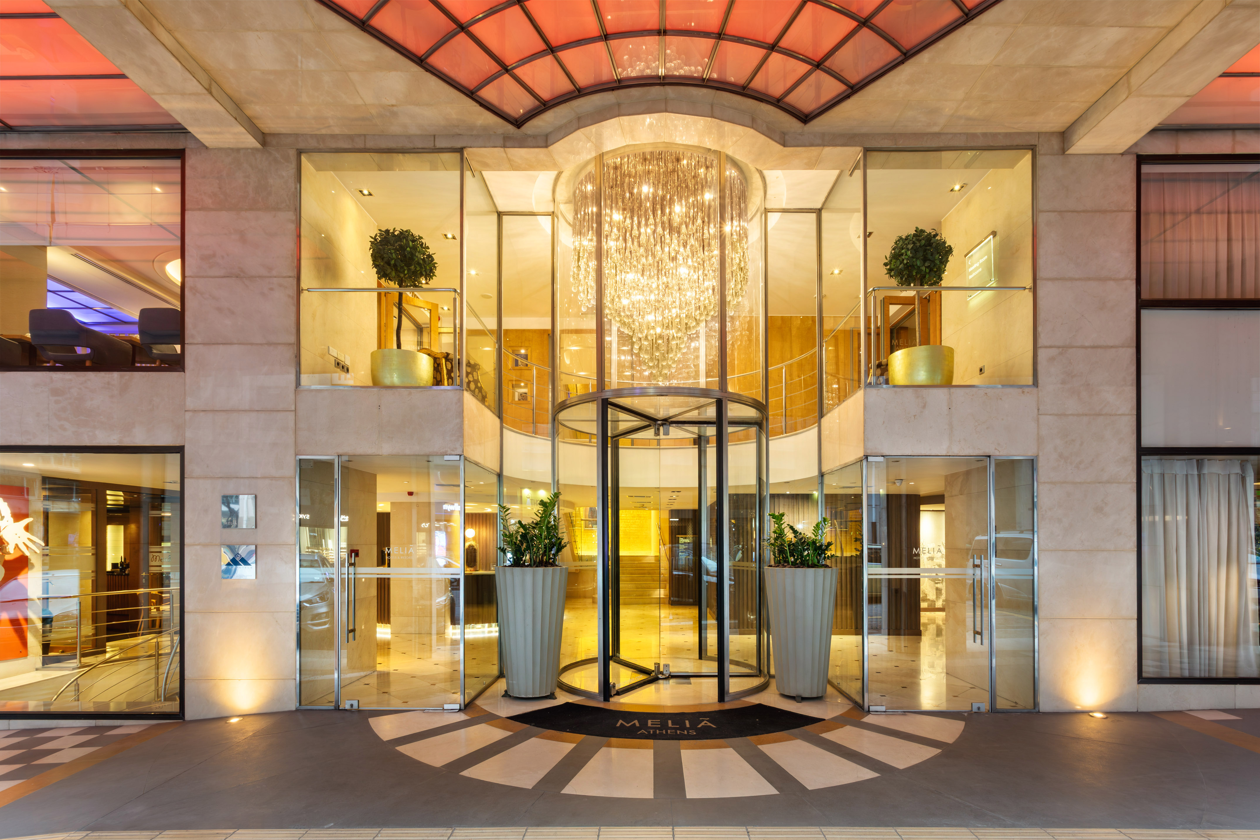 Meliá Athens luxury hotel entrance with revolving door and glowing chandelier.