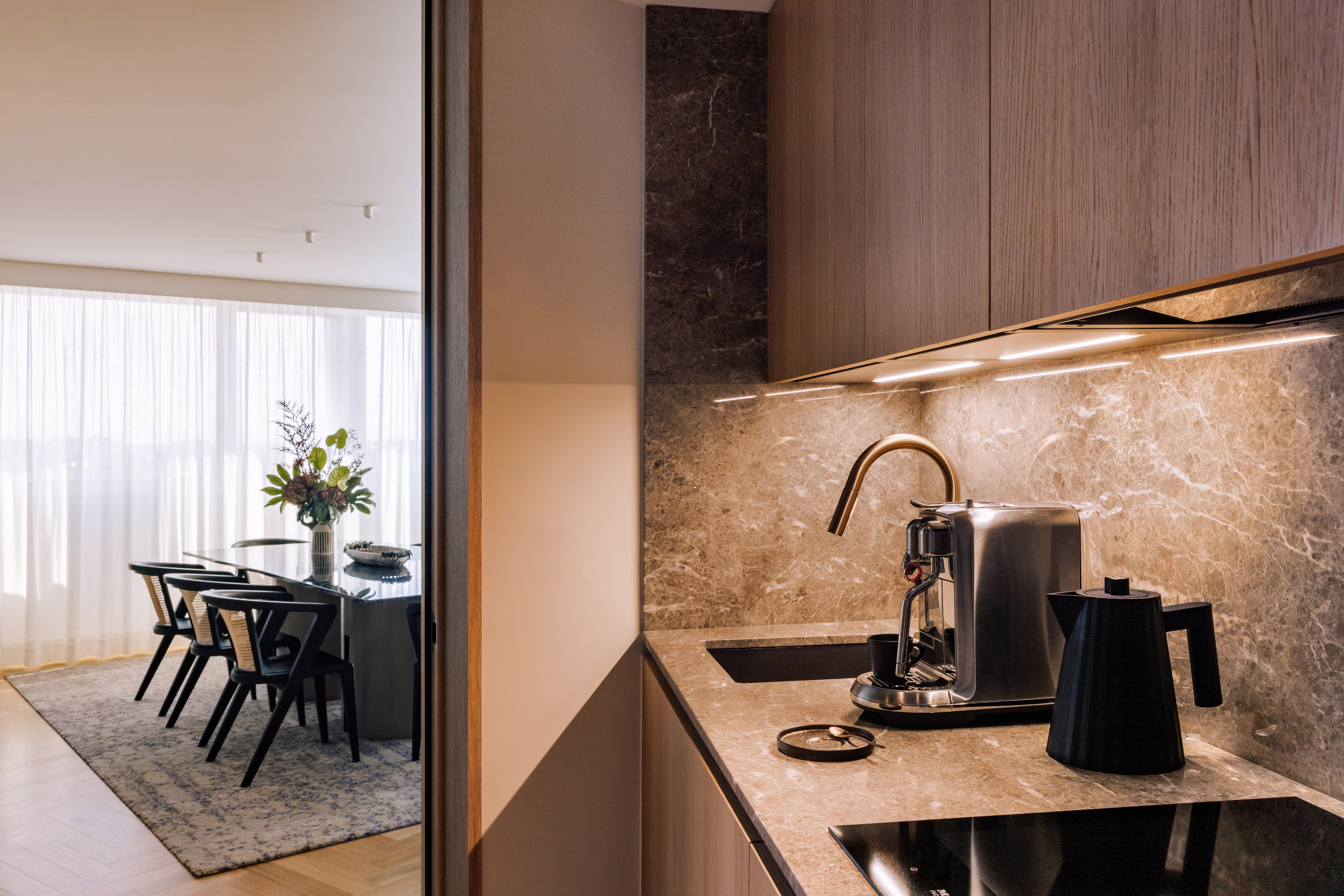 Modern kitchen with coffee maker, marble surfaces, and dining area with black table.
