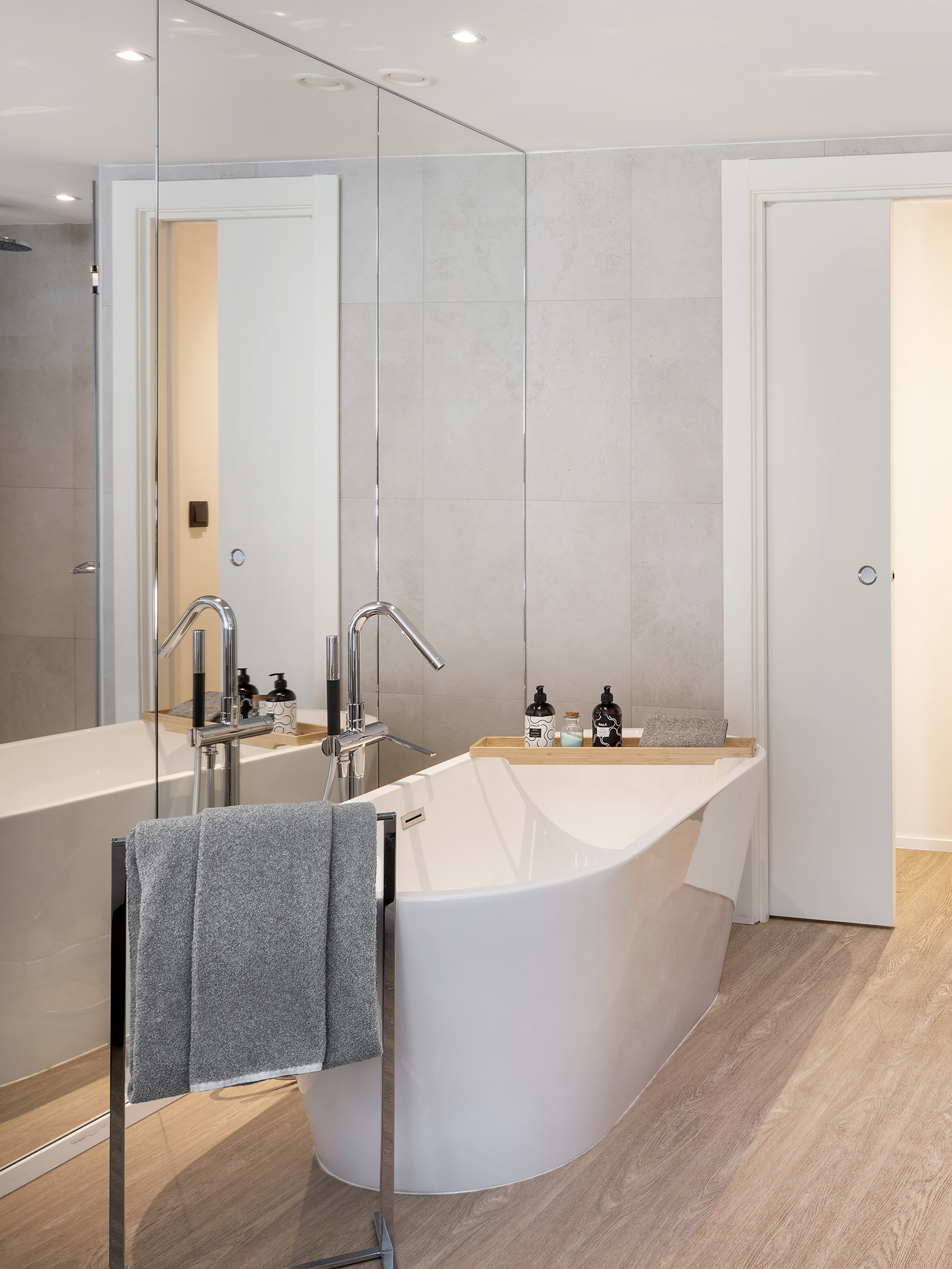 Modern bathroom, white freestanding tub, chrome faucet, grey tiles, wood floor.