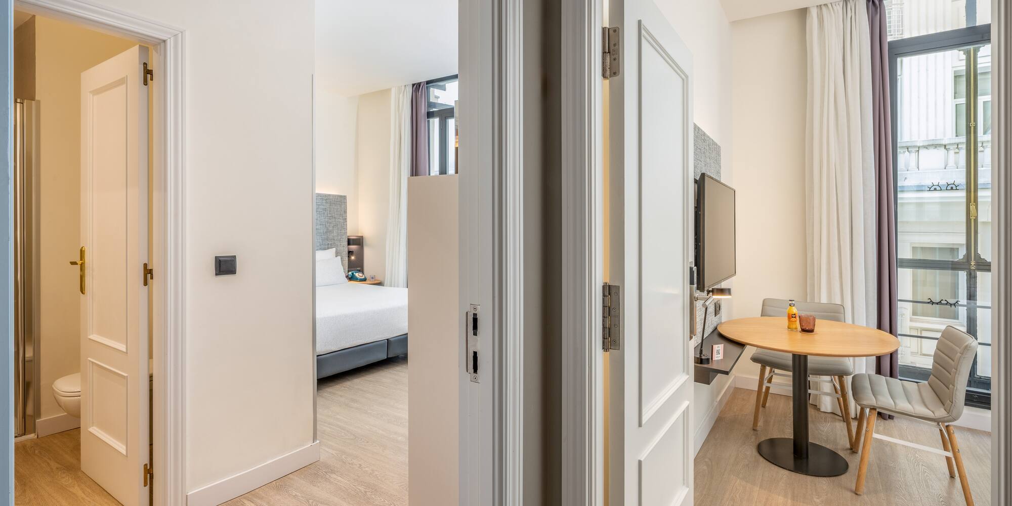 Bright hotel suite with bedroom, dining area, and bathroom.