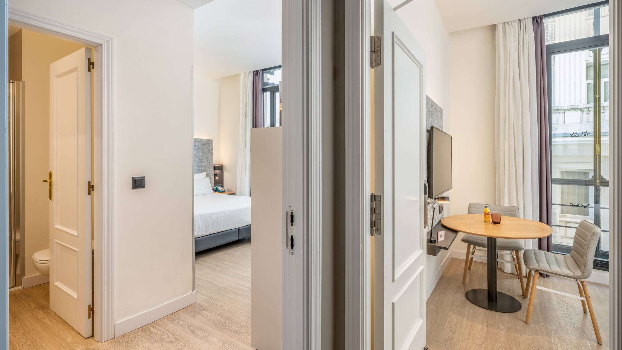 Bright hotel suite with bedroom, dining area, and bathroom.