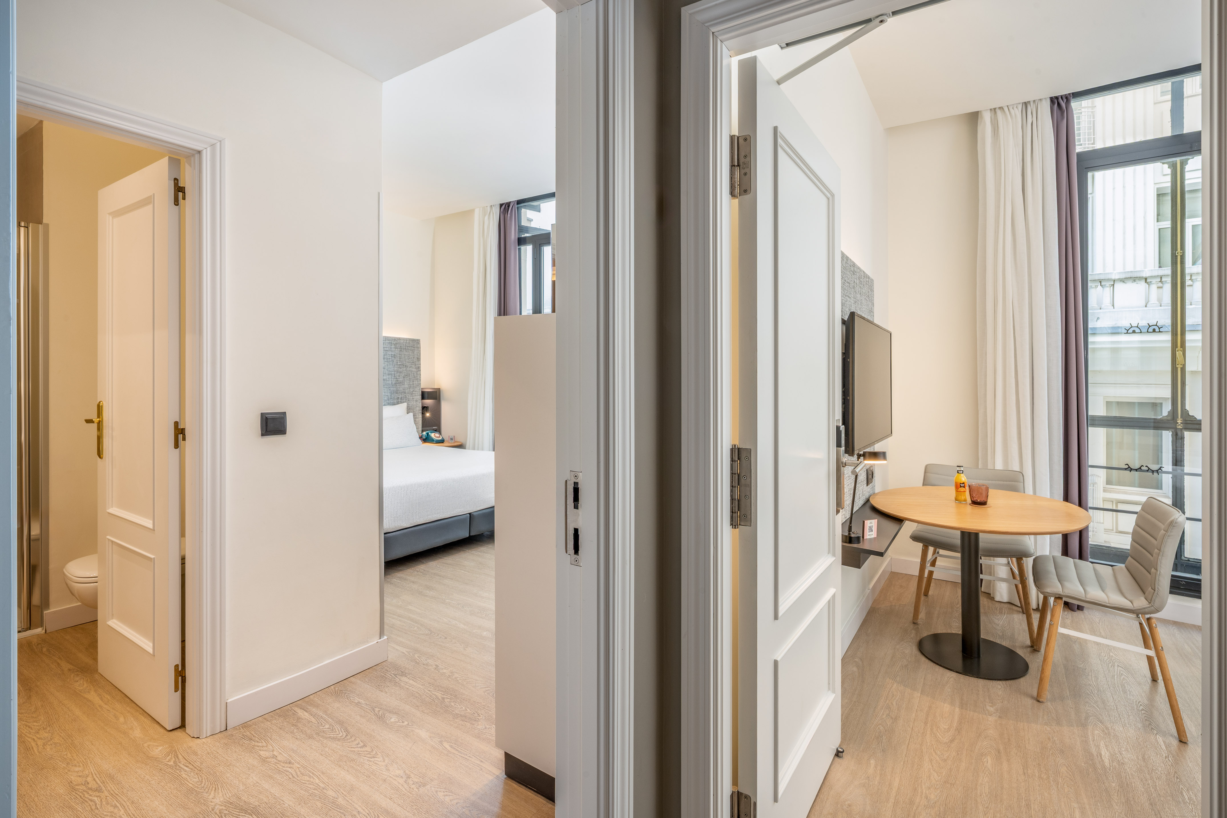 Bright hotel suite with bedroom, dining area, and bathroom.