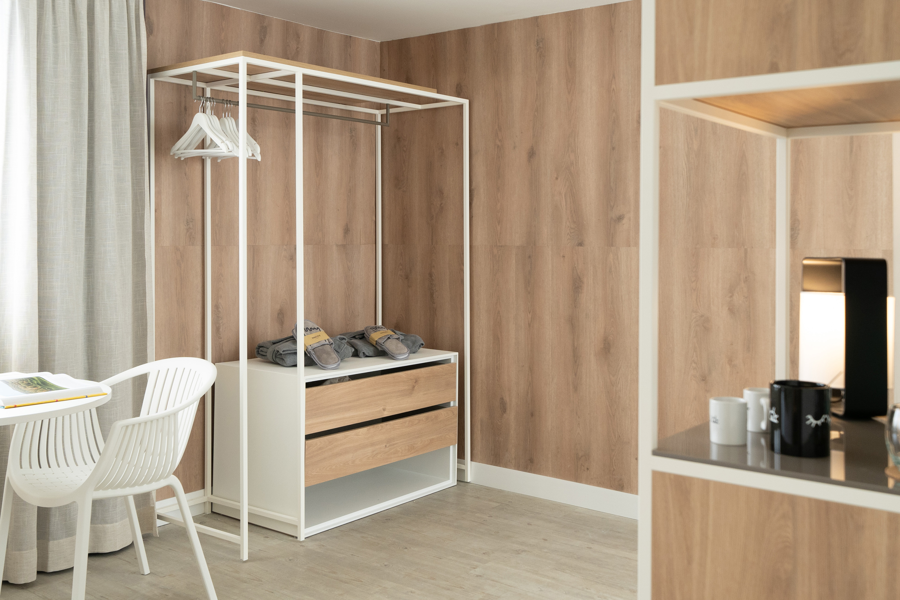 Modern hotel room with open wardrobe, wooden drawers, and minimalist design.