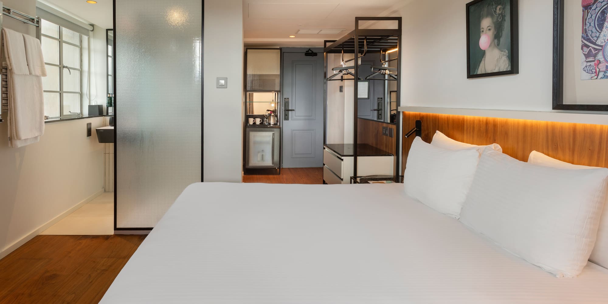 Modern hotel room with king bed, frosted glass shower, and compact kitchenette.