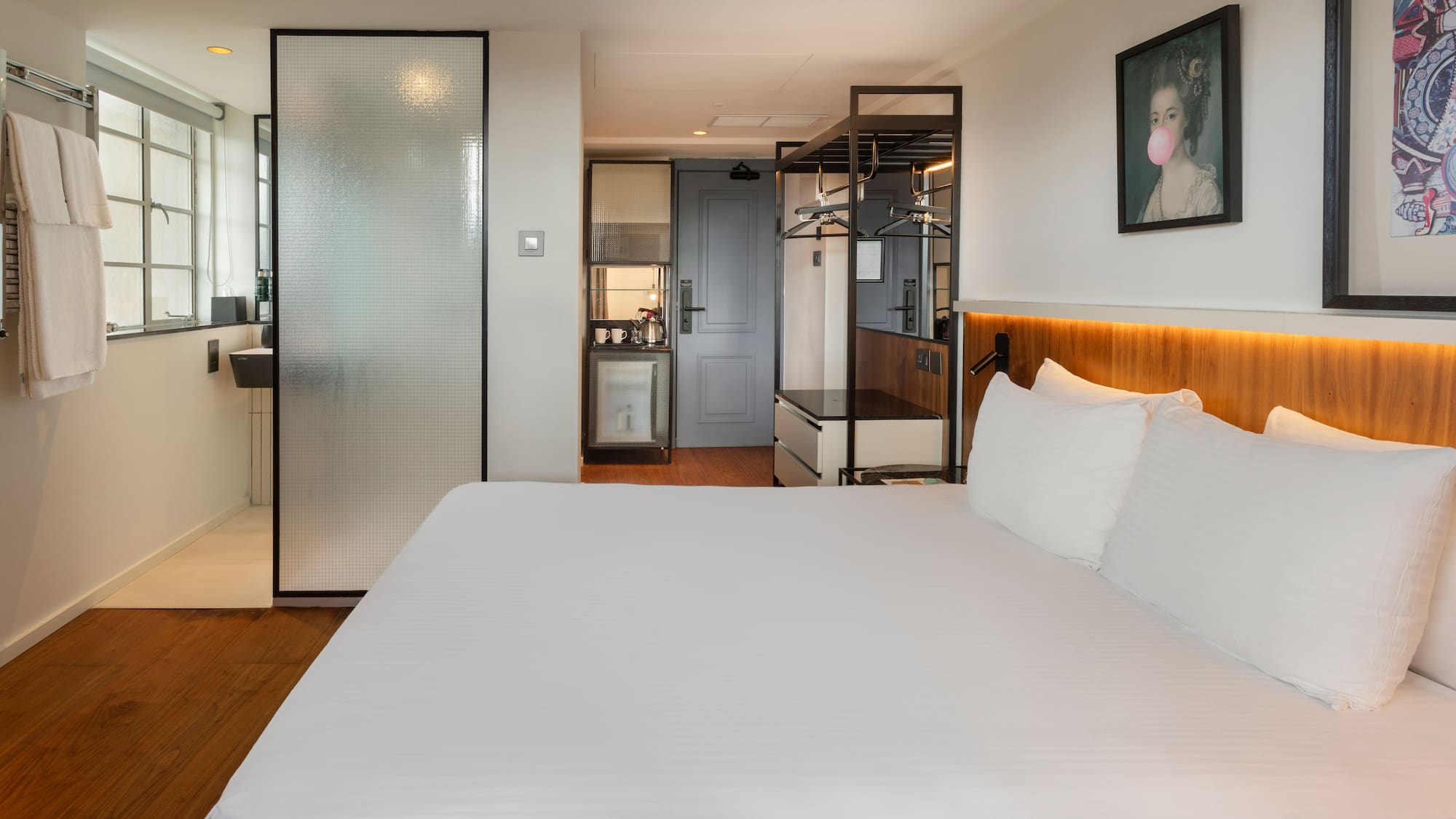 Modern hotel room with king bed, frosted glass shower, and compact kitchenette.