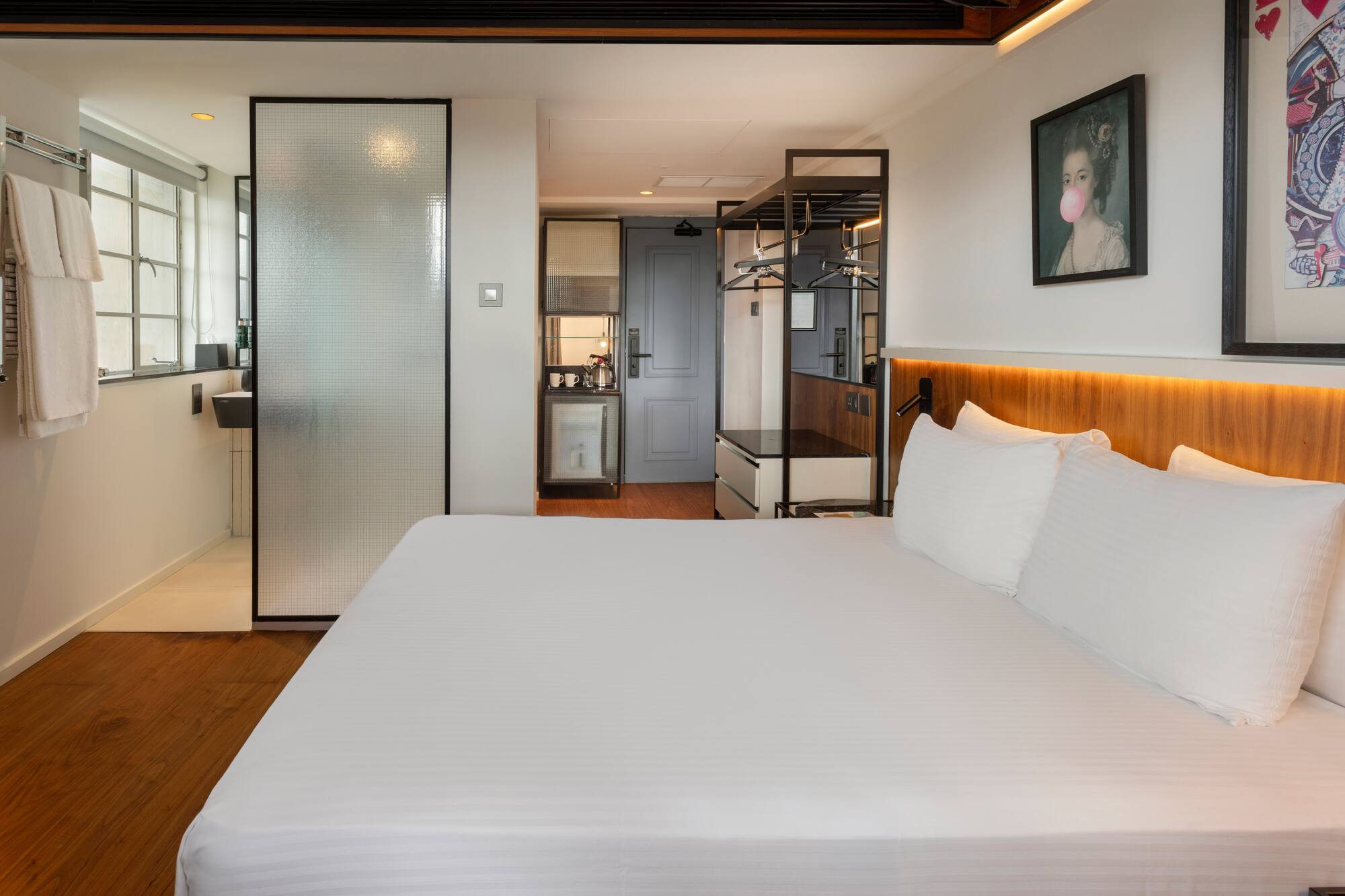 Modern hotel room with king bed, frosted glass shower, and compact kitchenette.