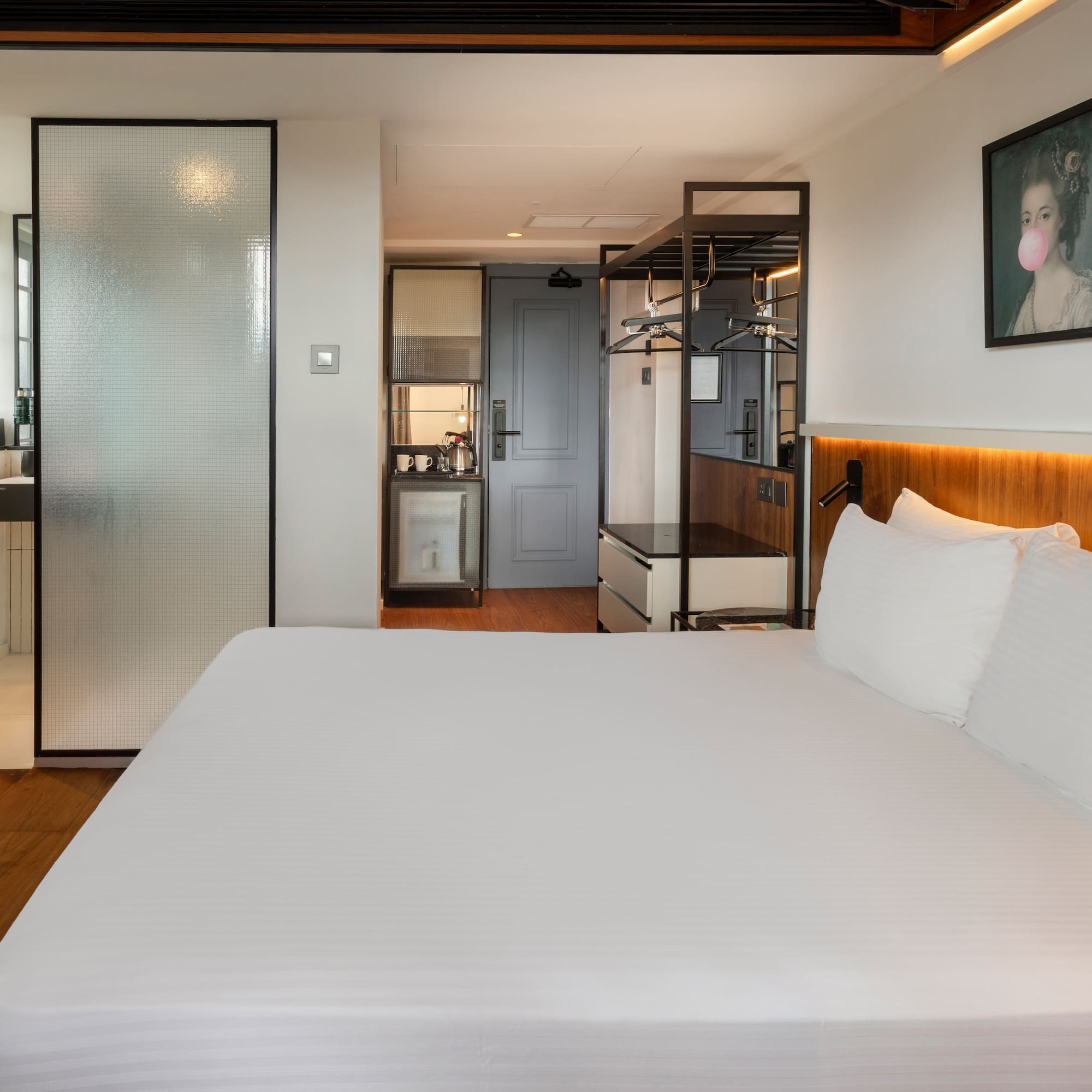 Modern hotel room with king bed, frosted glass shower, and compact kitchenette.