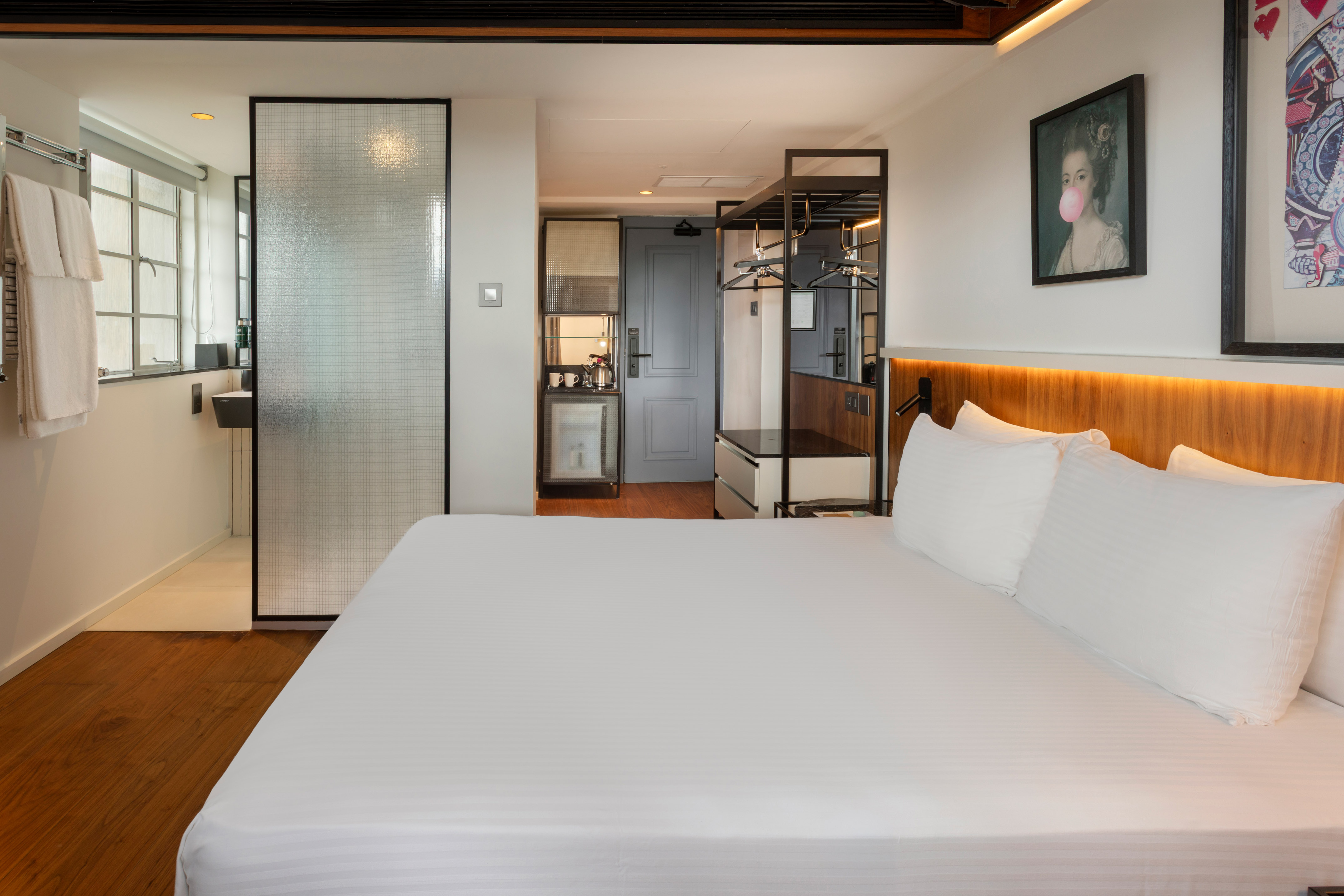 Modern hotel room with king bed, frosted glass shower, and compact kitchenette.