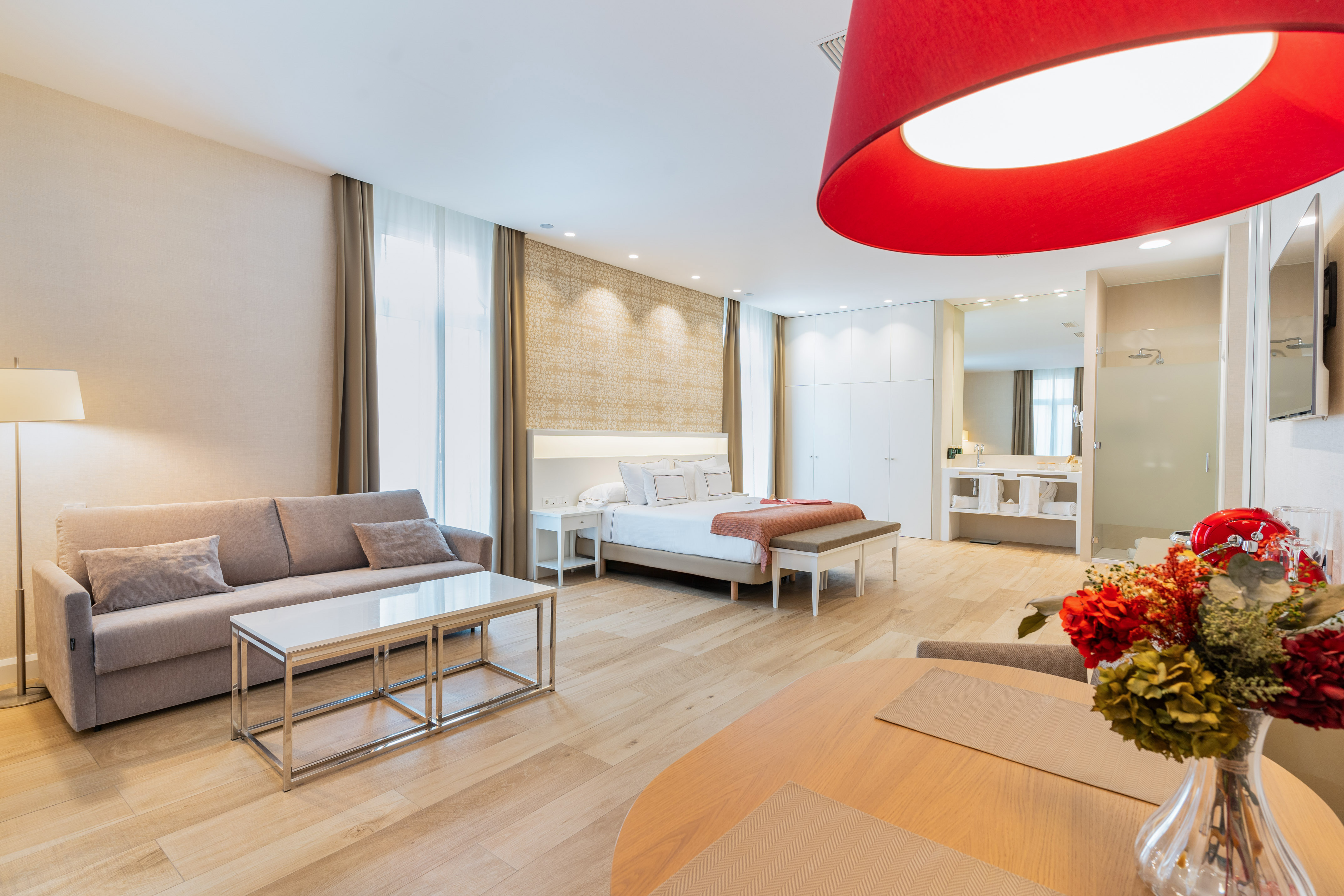 Spacious modern hotel suite with bed, sofa, dining, and bathroom area.