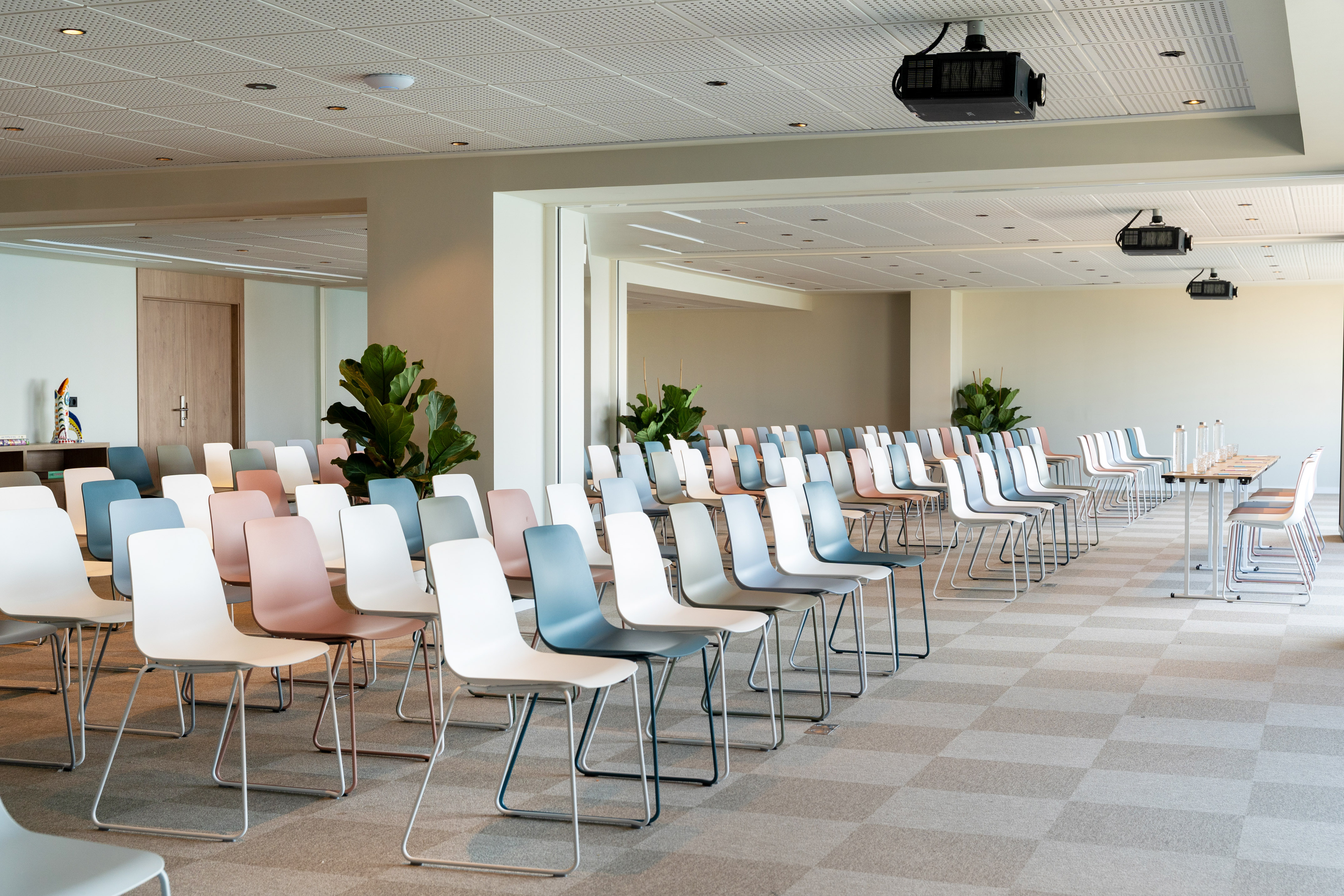 Empty modern conference room with colorful chairs, ceiling projectors, and tables.