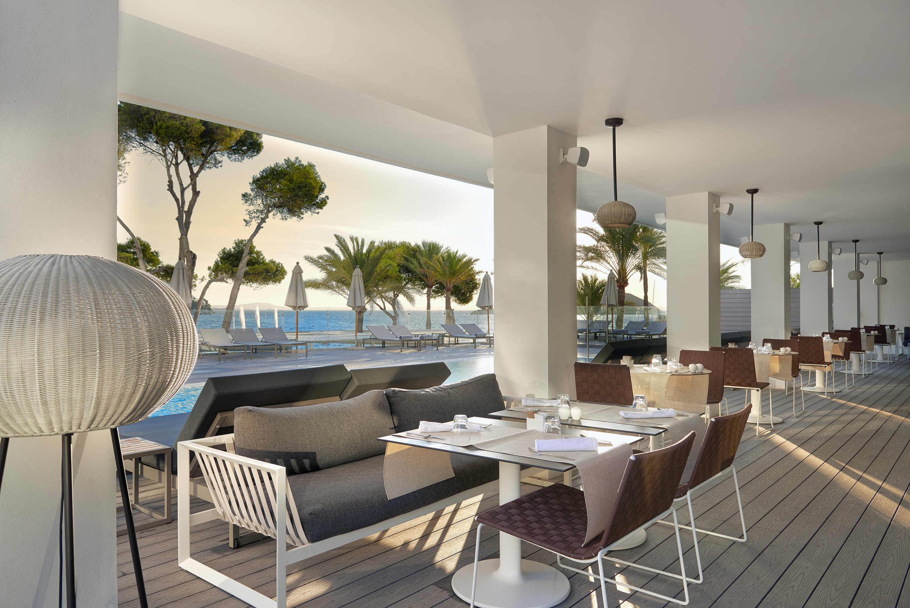 Modern outdoor restaurant terrace overlooking ocean and pool with palm trees.