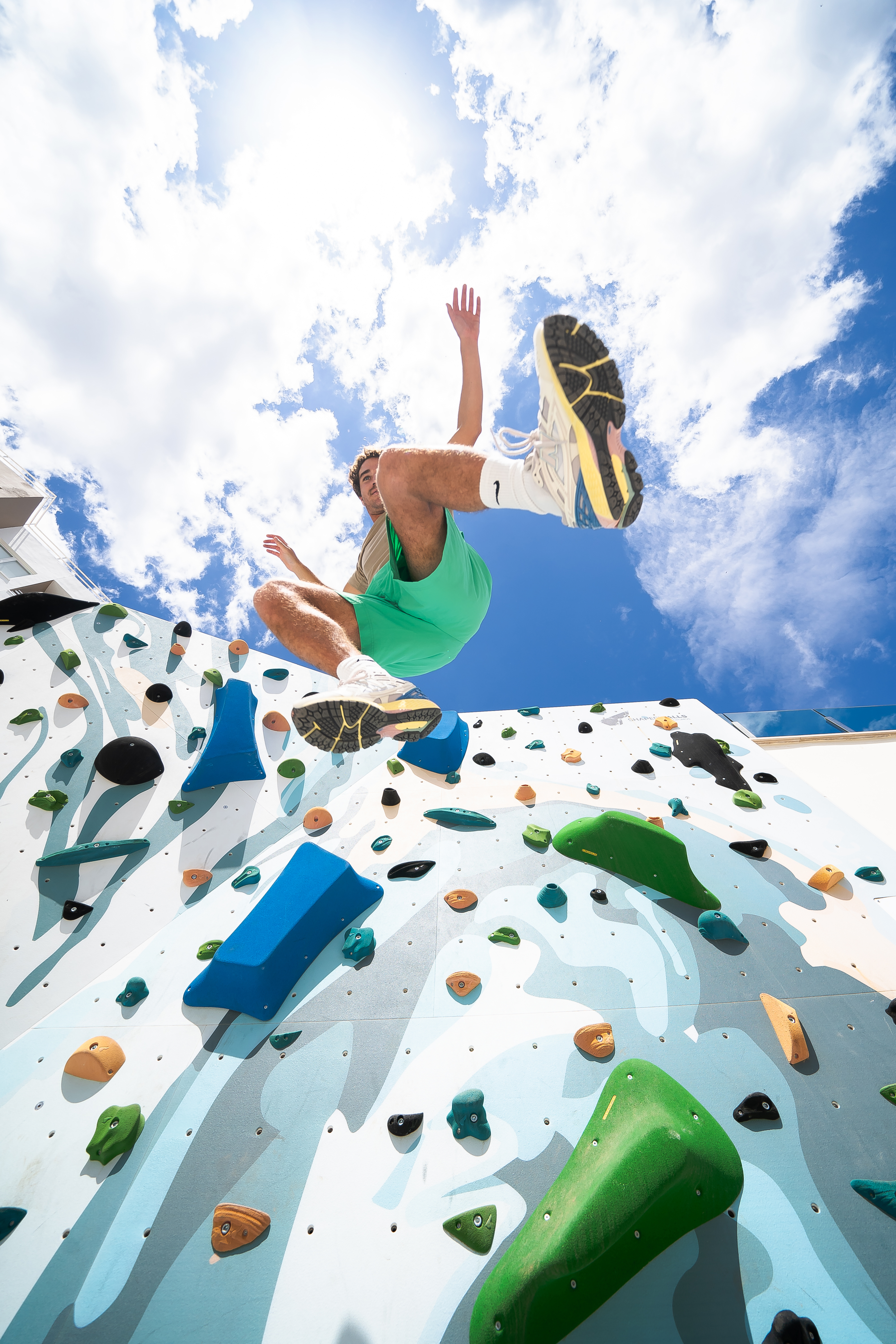 Athletic man bouldering on a colorful outdoor climbing wall under blue sky.