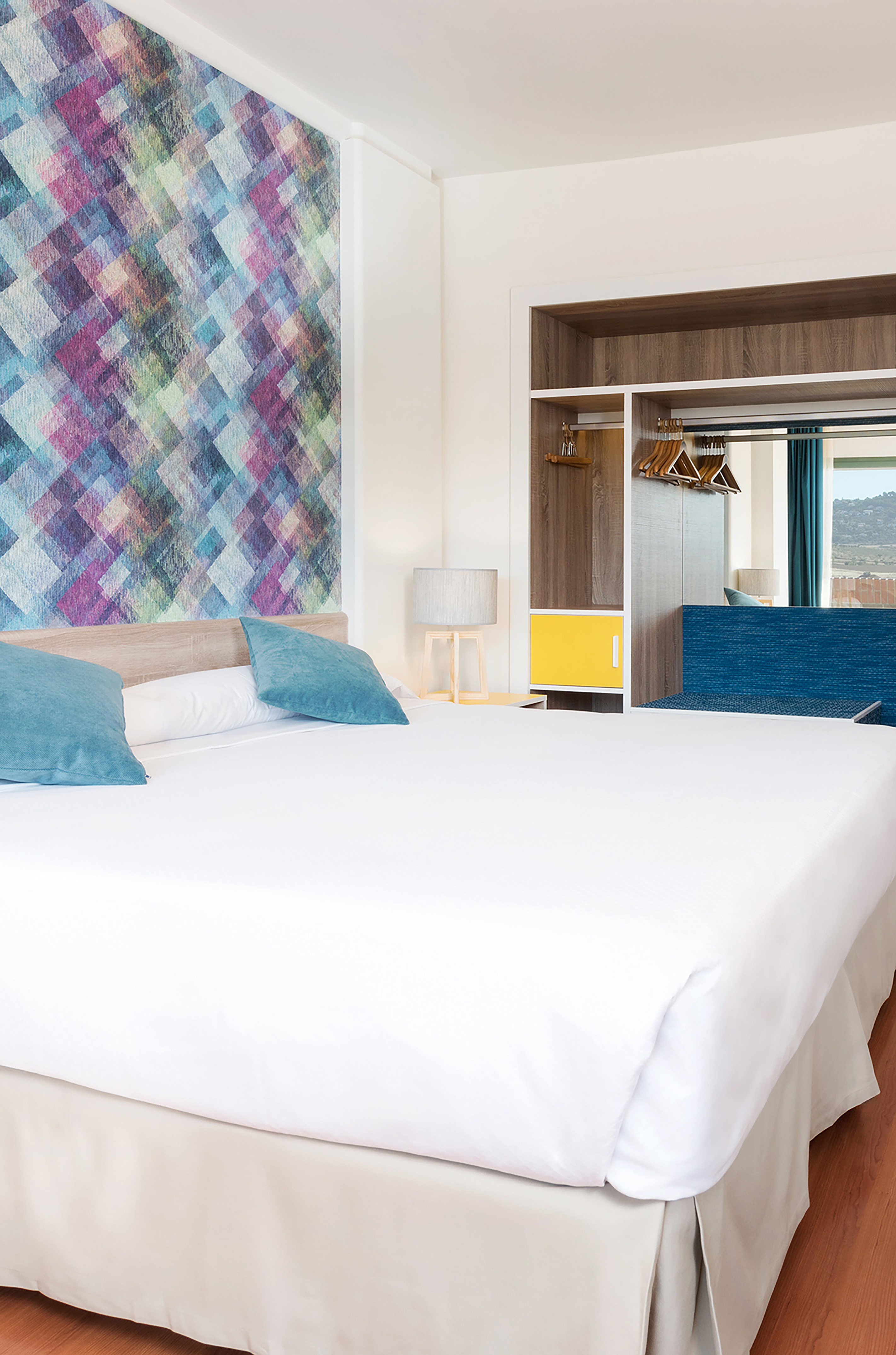 Modern bedroom with vibrant geometric wallpaper, white bed, and open closet.