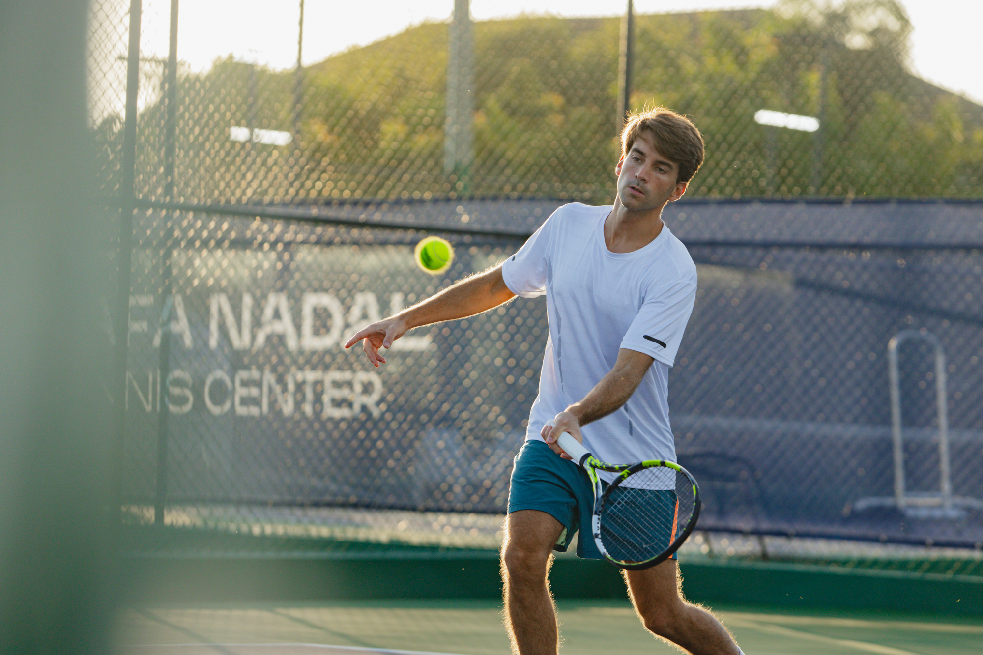 Male tennis player in action, mid-swing hitting ball at Nadal Tennis Center.