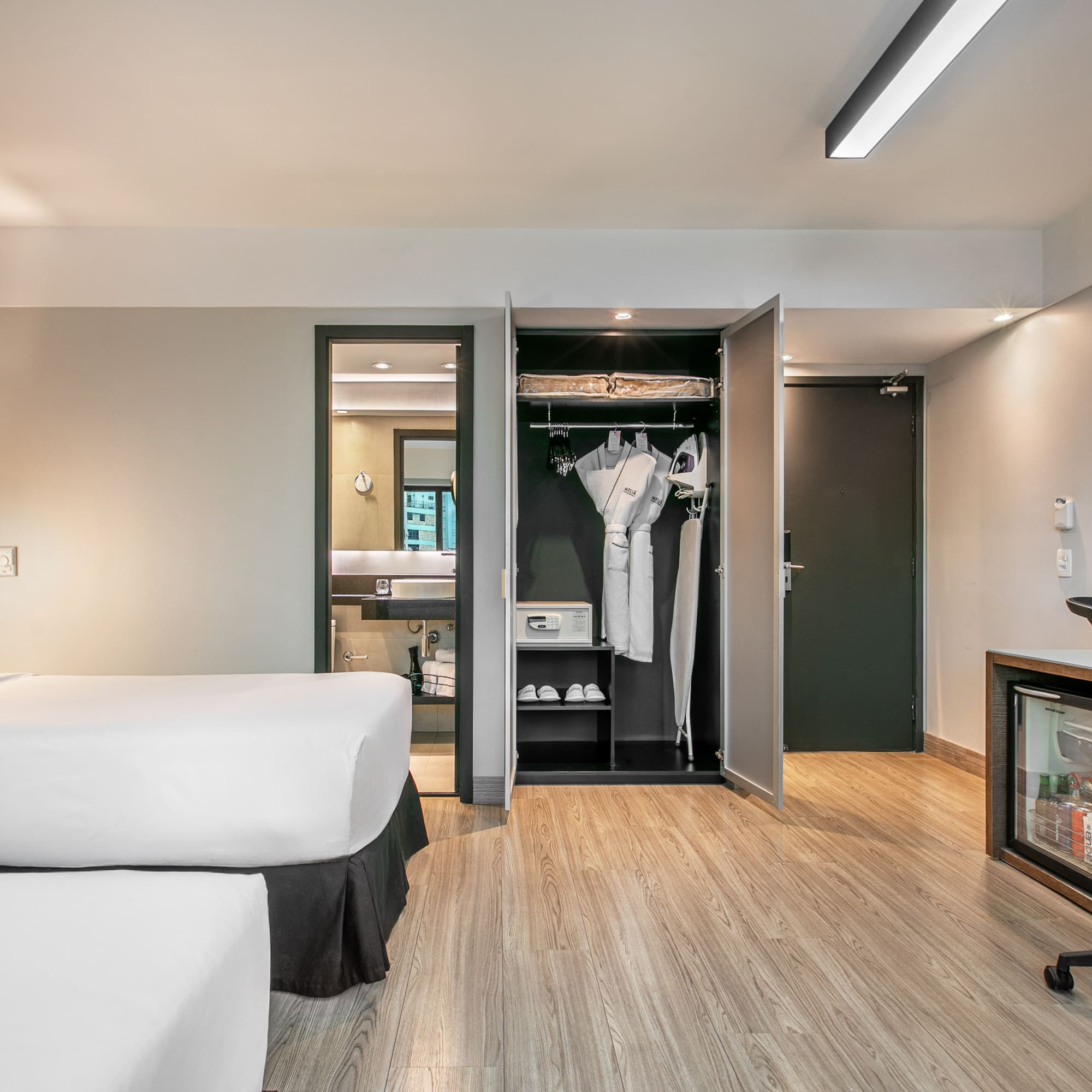 Quarto de hotel moderno com duas camas, armário aberto e mesa de trabalho. - Deluxe Room Twin - Meliá Ibirapuera, São Paulo