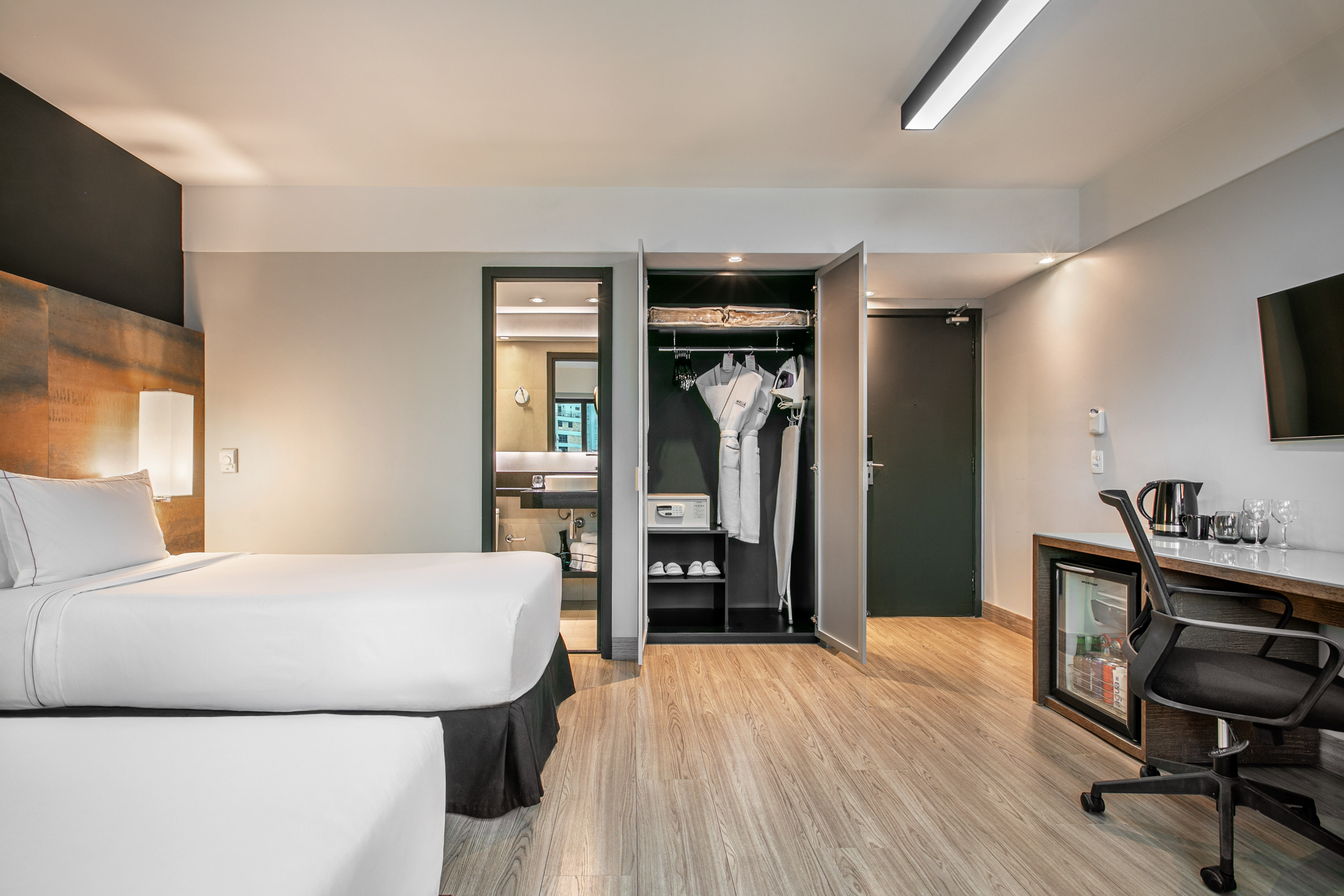 Quarto de hotel moderno com duas camas, armário aberto e mesa de trabalho. - Deluxe Room Twin - Meliá Ibirapuera, São Paulo