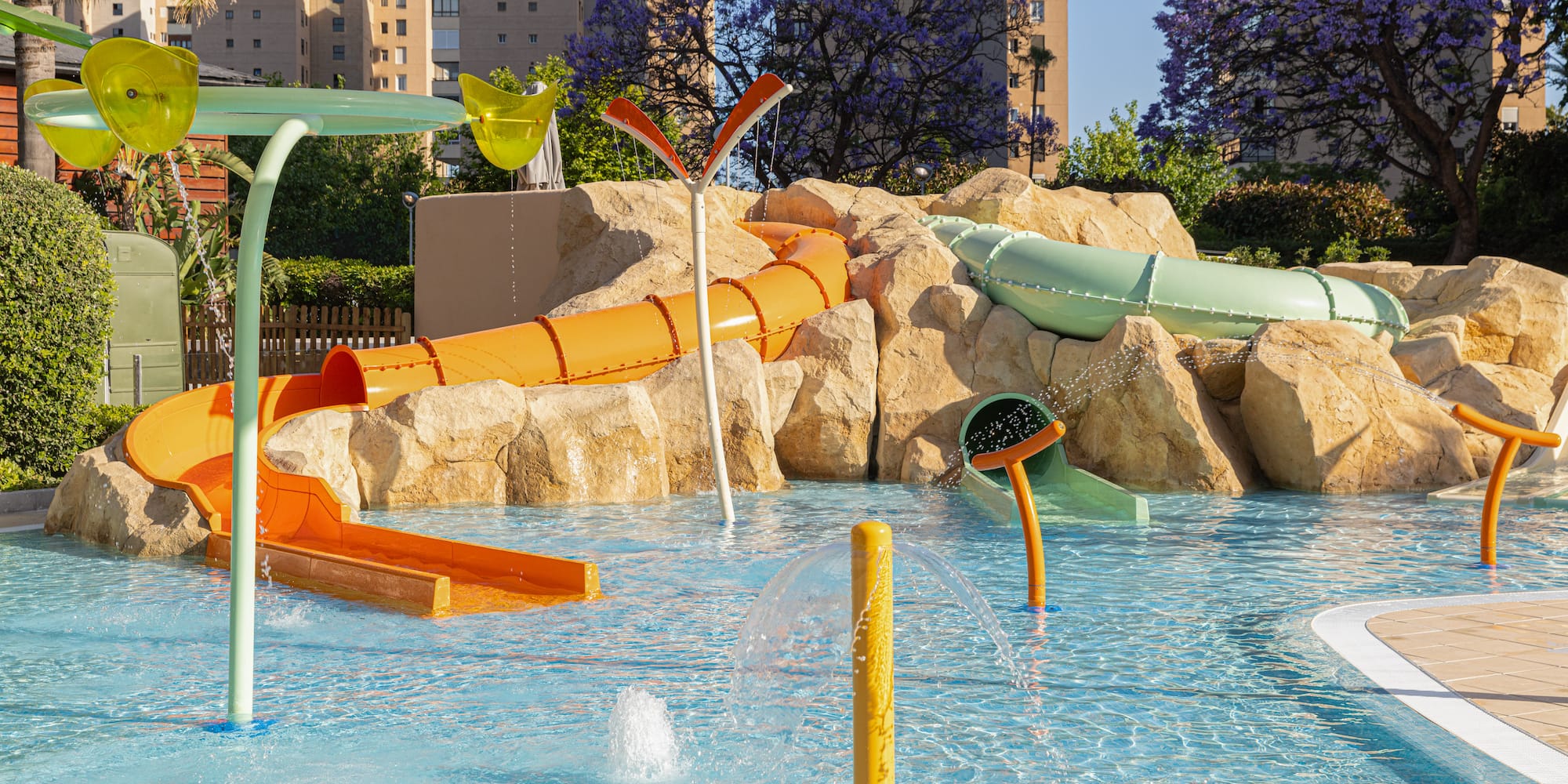 Kids' water park with colorful slides, splash pad, and rock features.