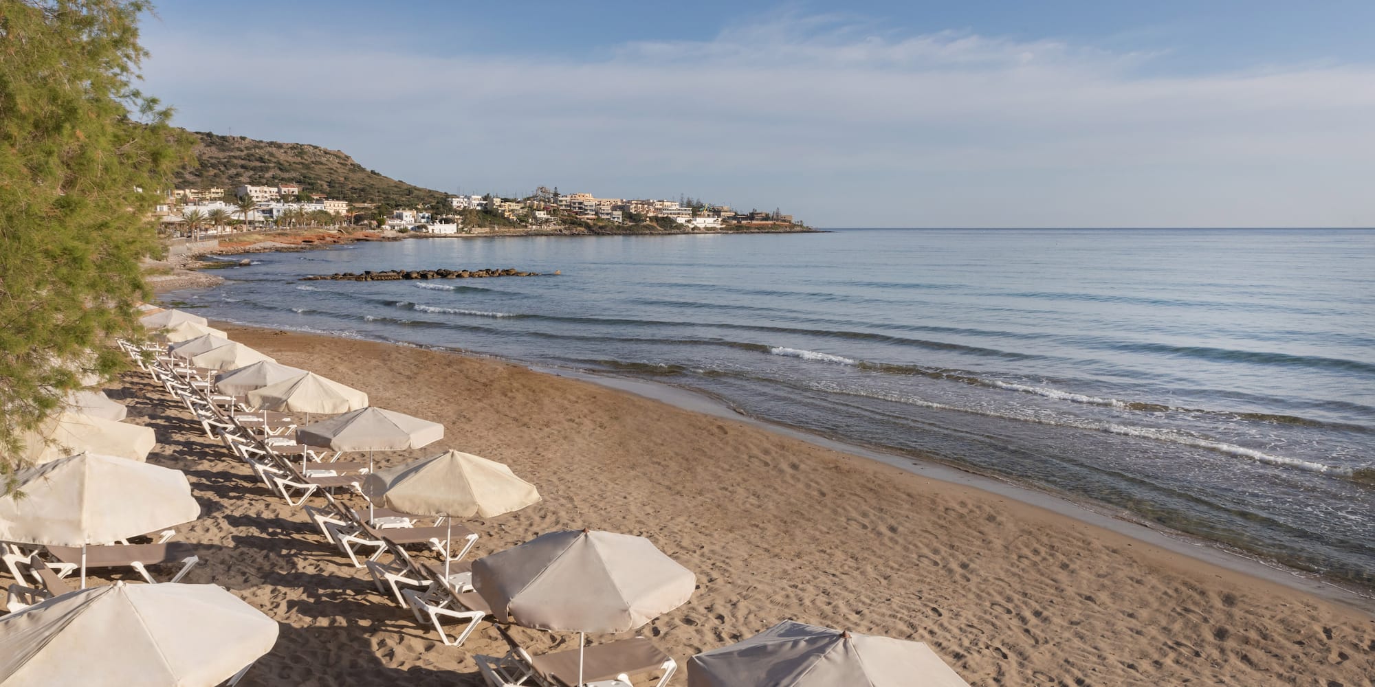 Beach with lounge chairs, parasols, calm sea, and coastal town.