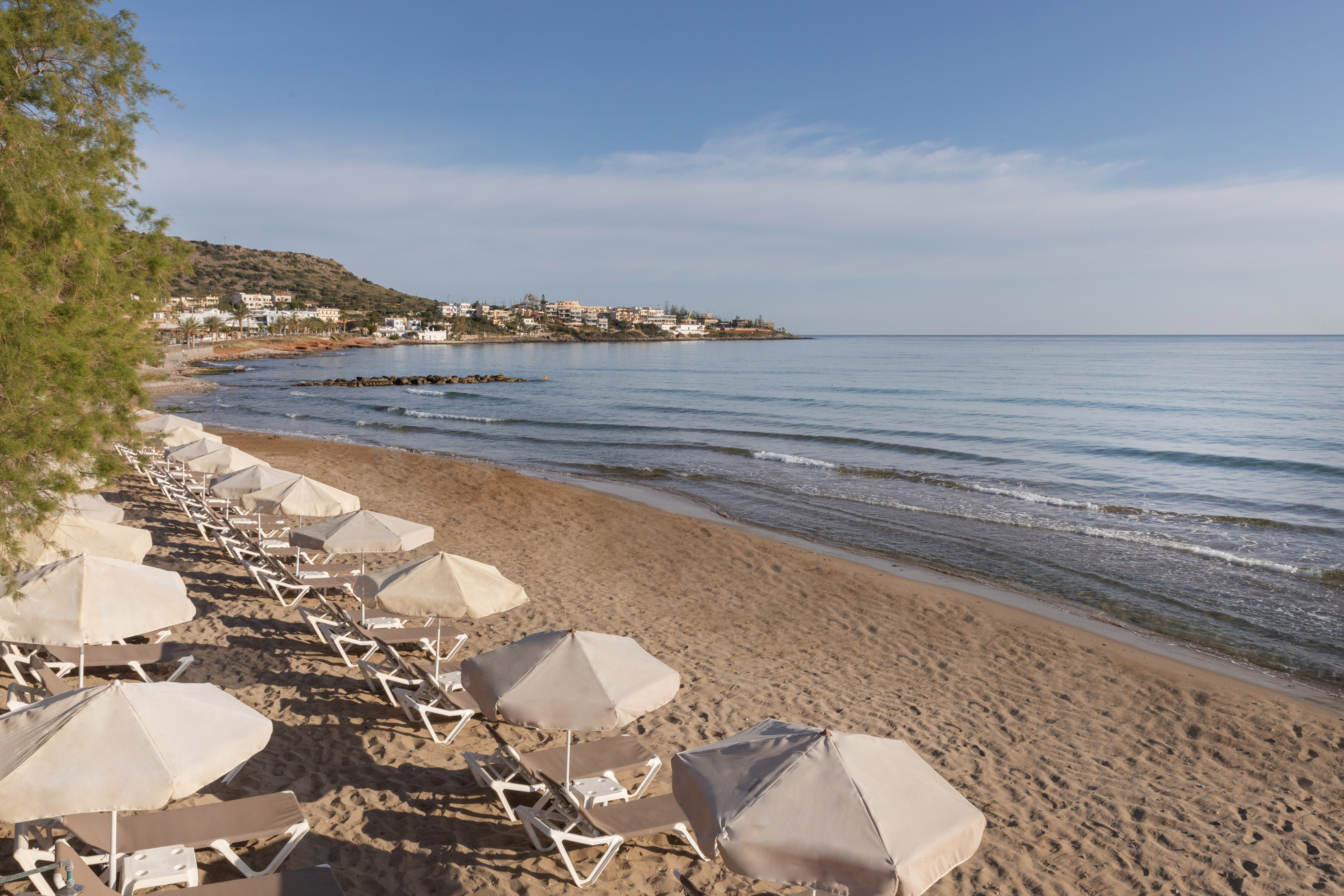 Beach with lounge chairs, parasols, calm sea, and coastal town.