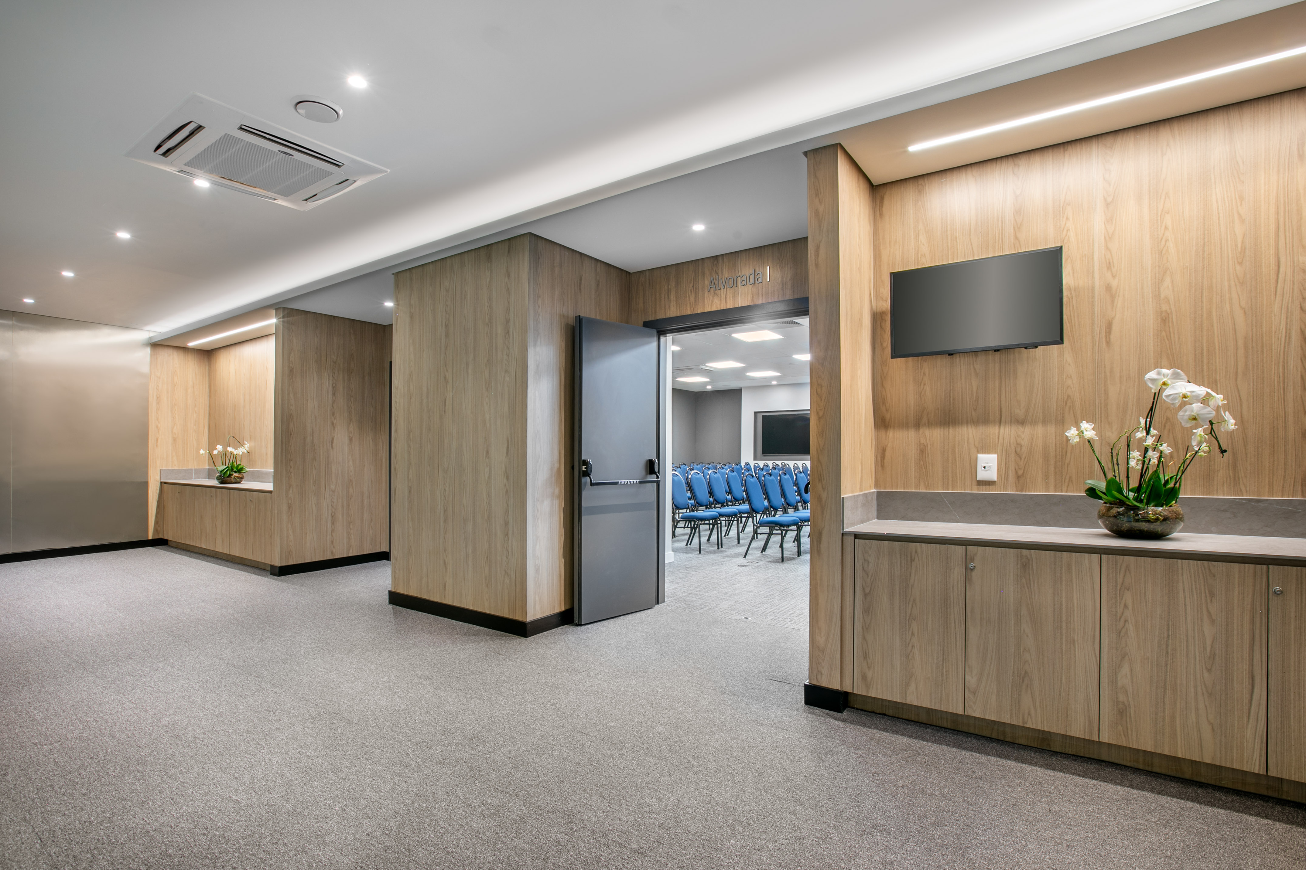 Corporate hallway to meeting room, wood paneling, TV, blue chairs visible.