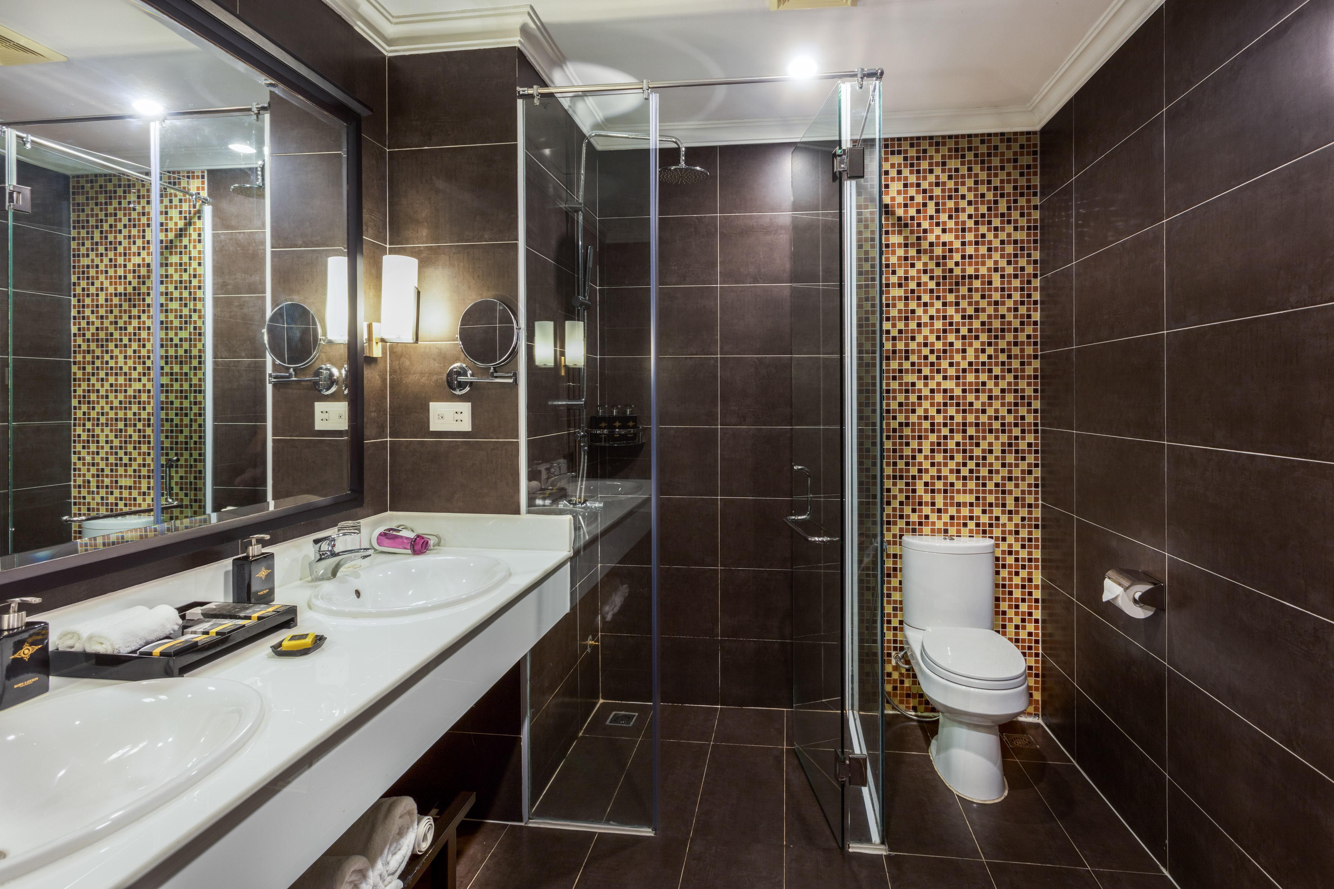 Dark tiled modern bathroom with double vanity, glass shower, and toilet.