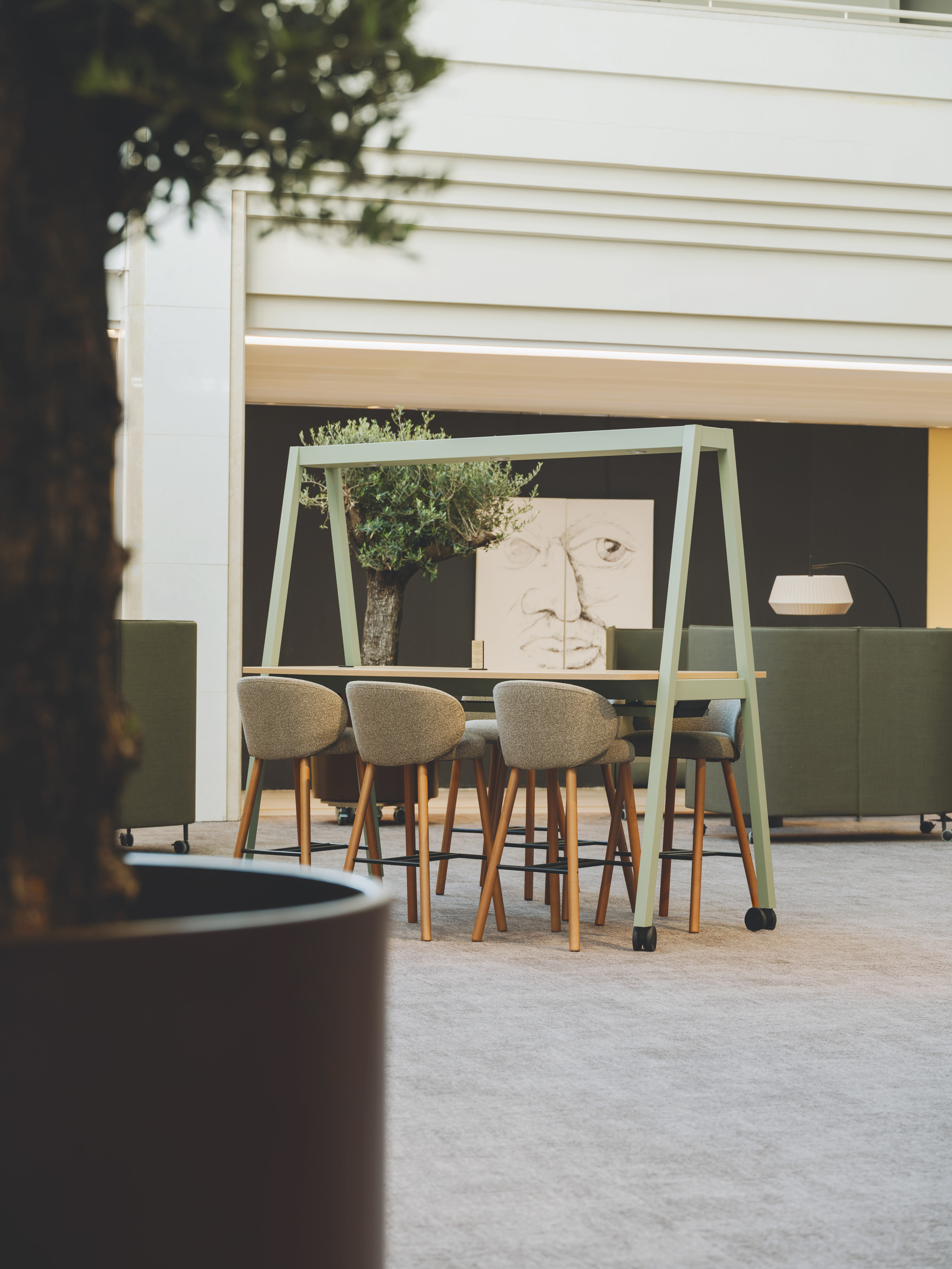Modern office collaboration table with green frame, gray chairs, and plant.