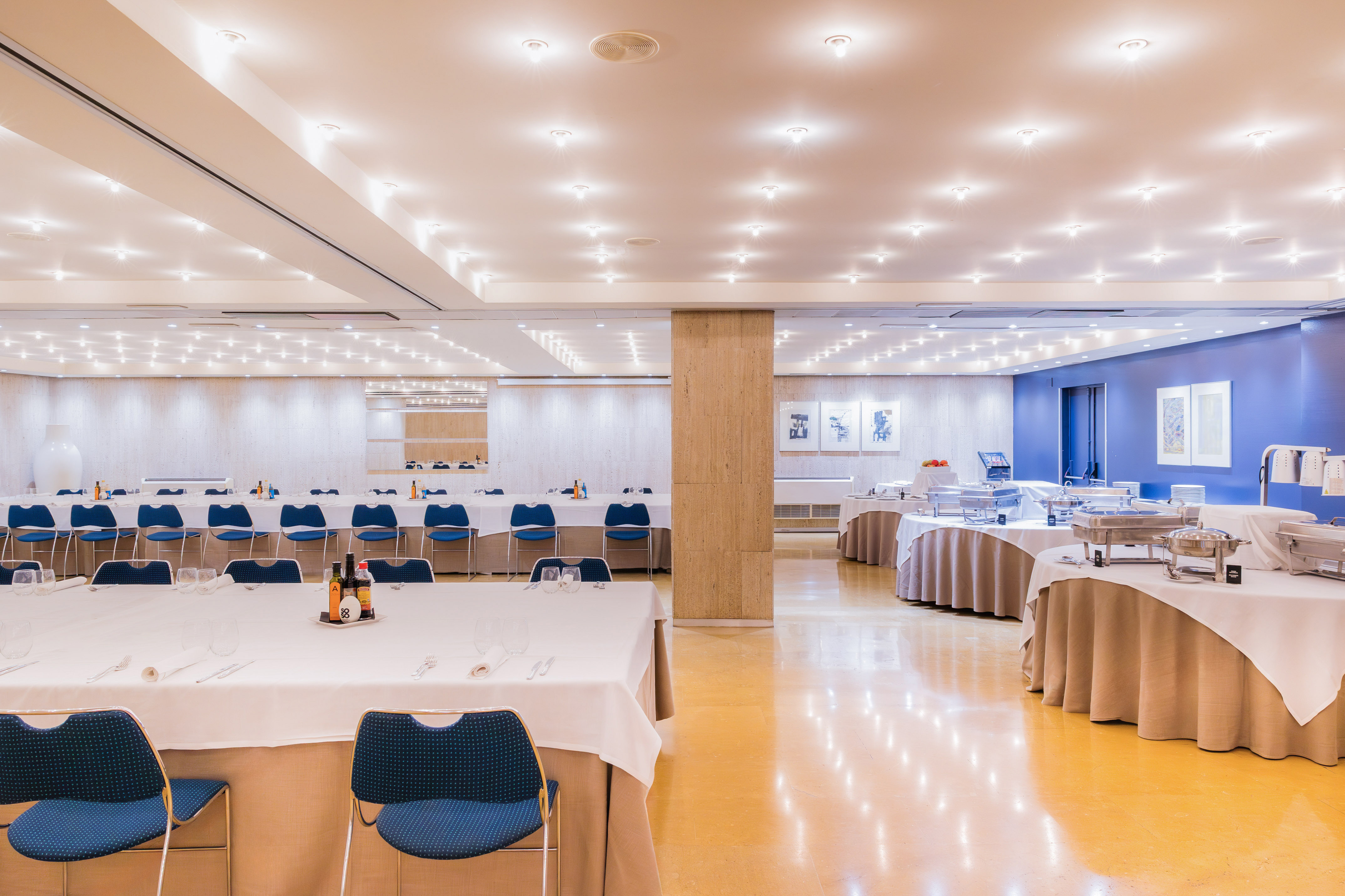 Spacious hotel banquet hall with set tables, blue chairs, and buffet.